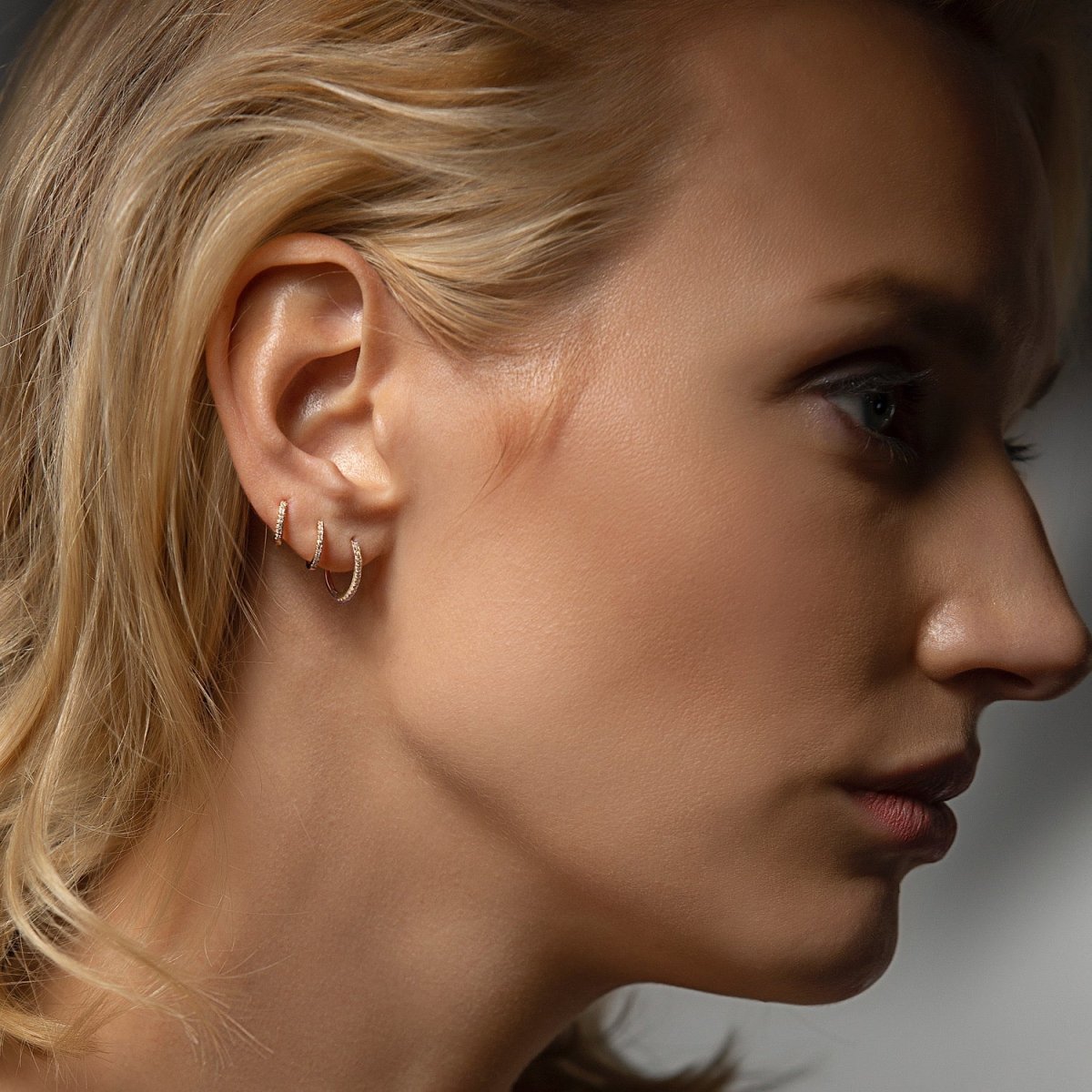14K white gold thin diamond huggie hoops stacked on a model's lobe