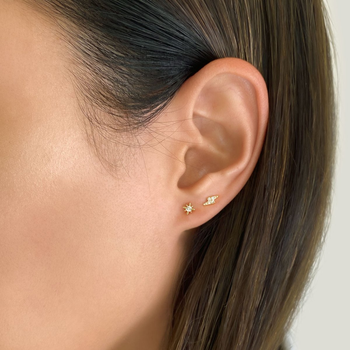 14K gold diamond lightning bolt stud beside a sun stud on a model's lobe
