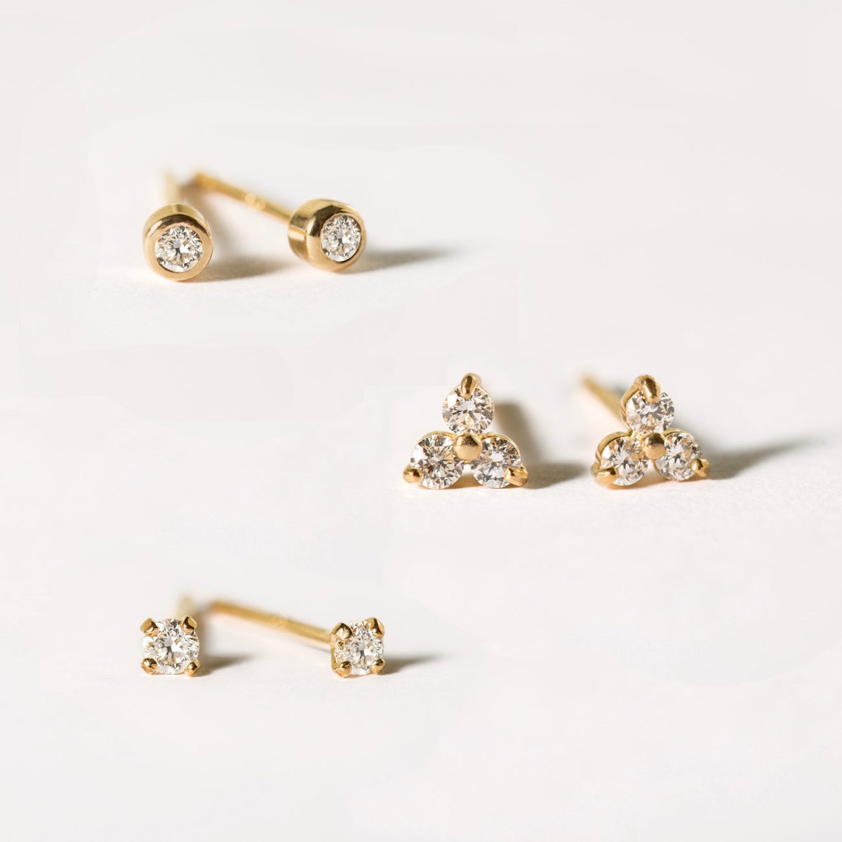 14K gold diamond stud earrings, a bezel pair and a three-stone cluster pair, on a white background