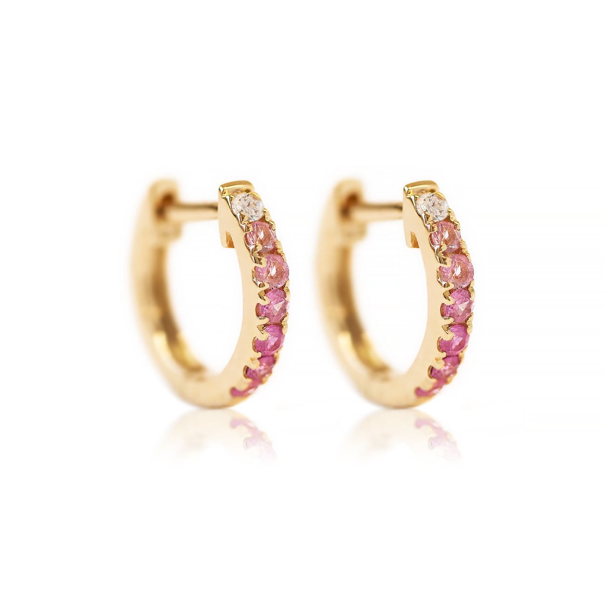 Pair of 14K gold huggie hoops pavé-set with ombre clear and pink sapphire stones, on a white background