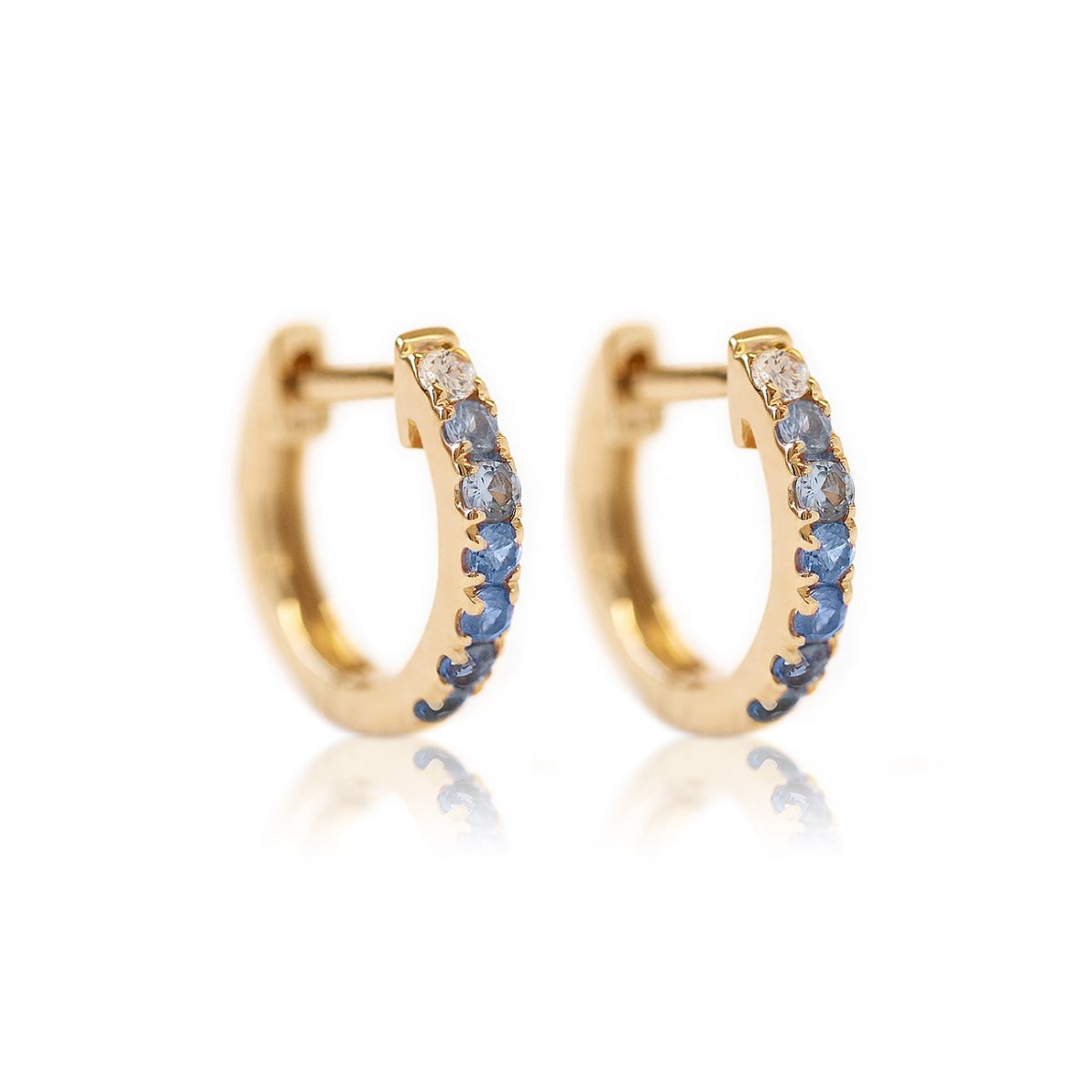 Pair of 14K gold huggie hoops pavé-set with ombre clear and blue sapphire stones, on a white background