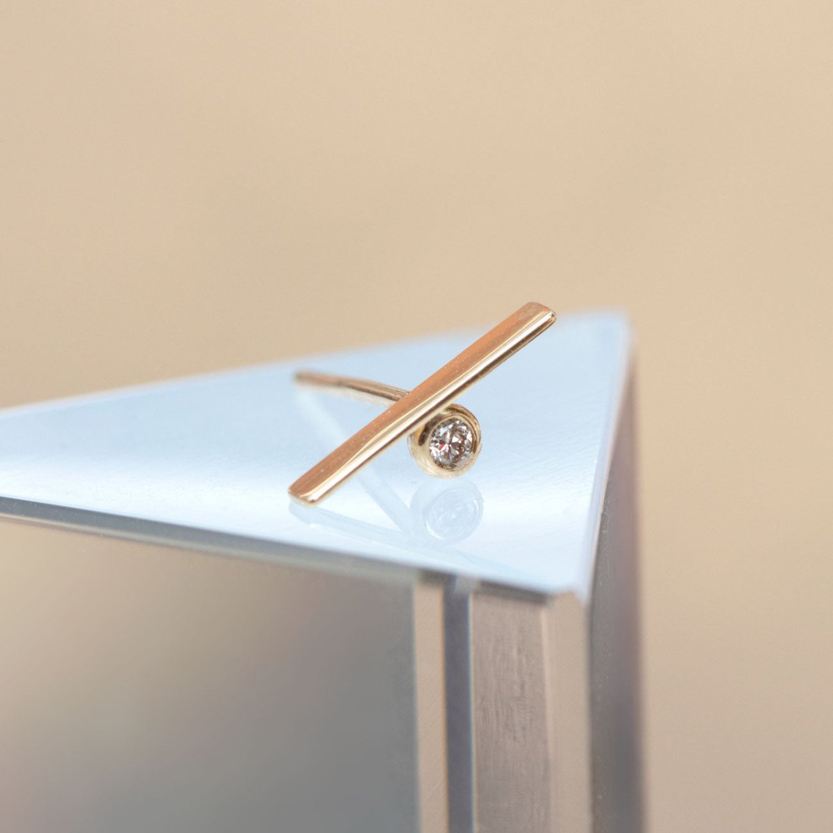14K gold bar stud with a small round diamond, shown on a pale surface