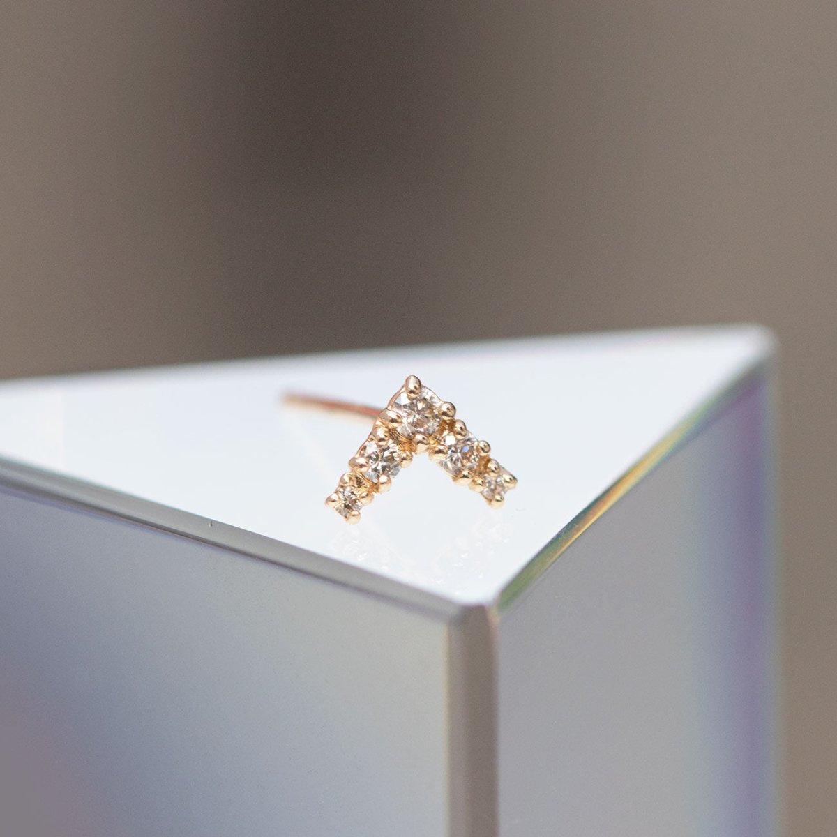 14K gold V-shaped chevron diamond stud shown close-up on a reflective white surface