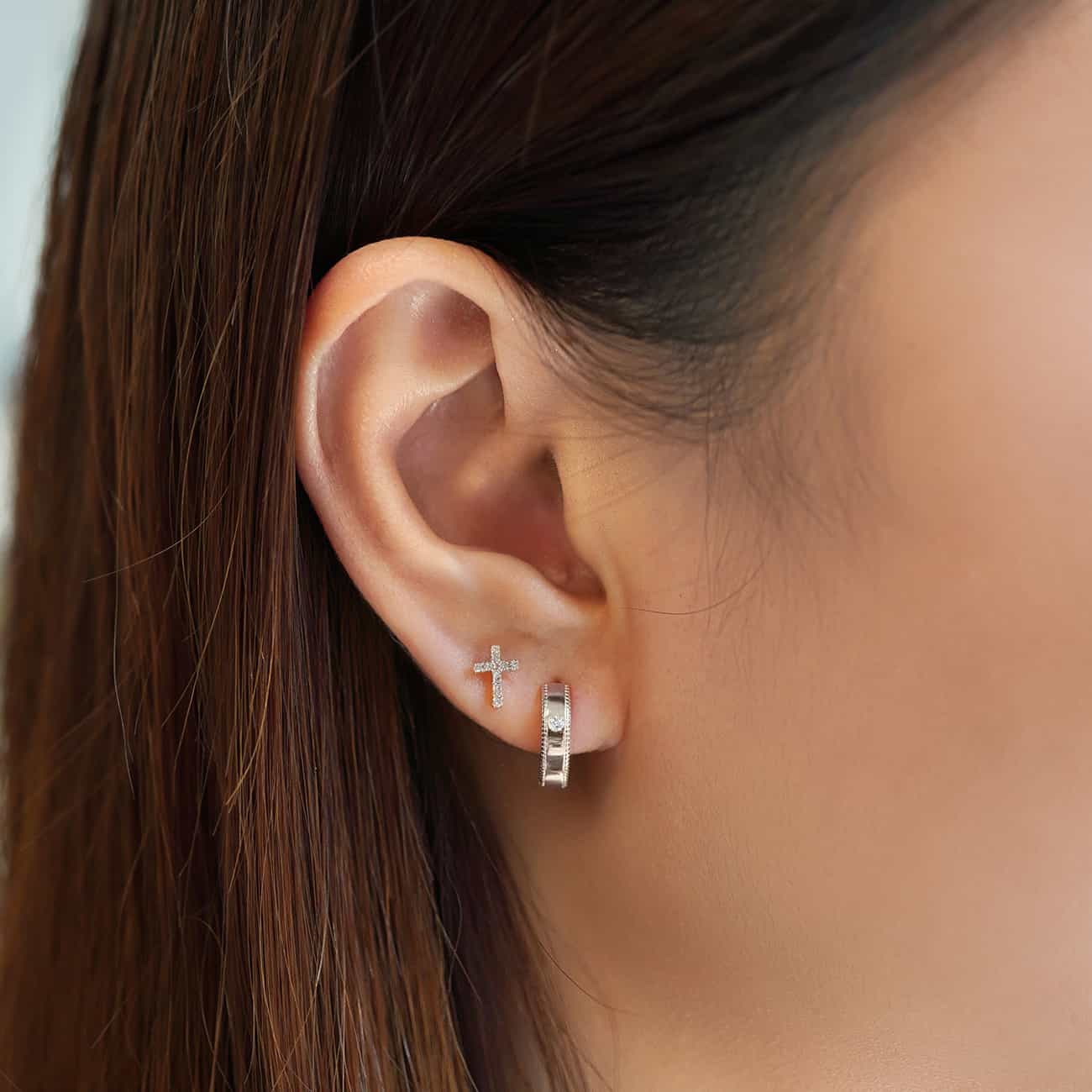 Silver pavé cross stud and a milgrain huggie hoop shown on a model's lobe