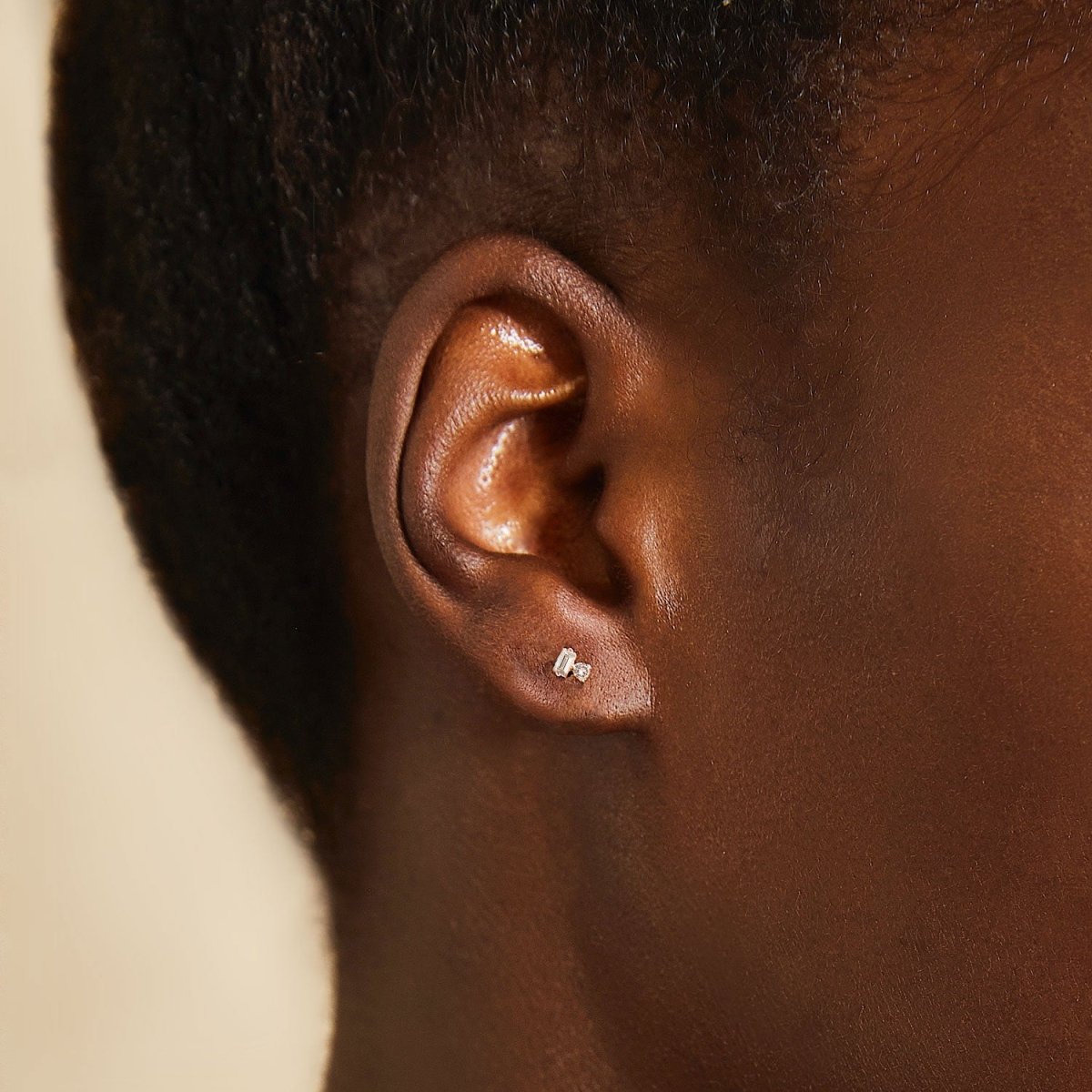14K rose gold baguette and round diamond duet stud shown close-up on a model's lobe