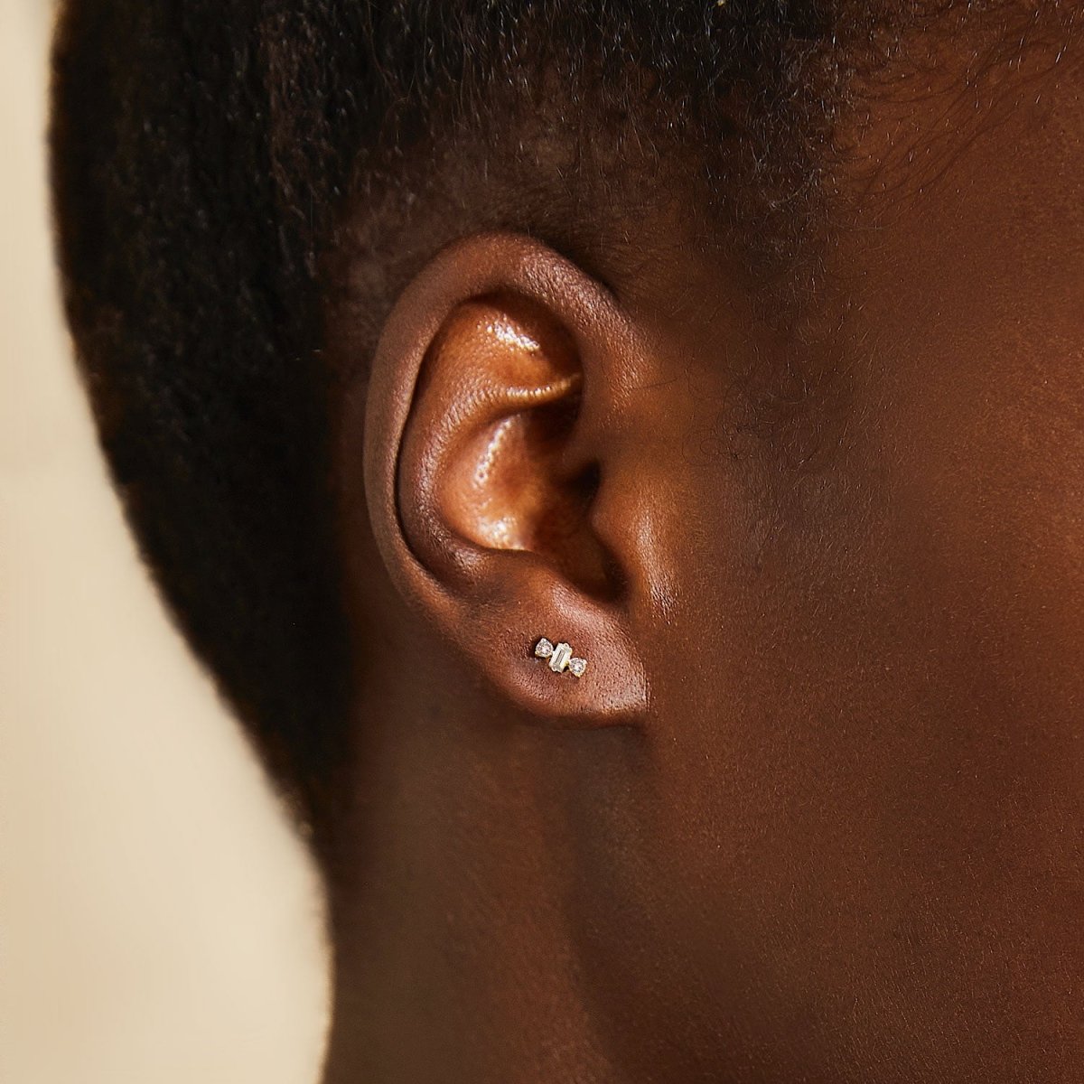 14K gold diamond baguette triad stud shown on a model's lobe, close-up detail