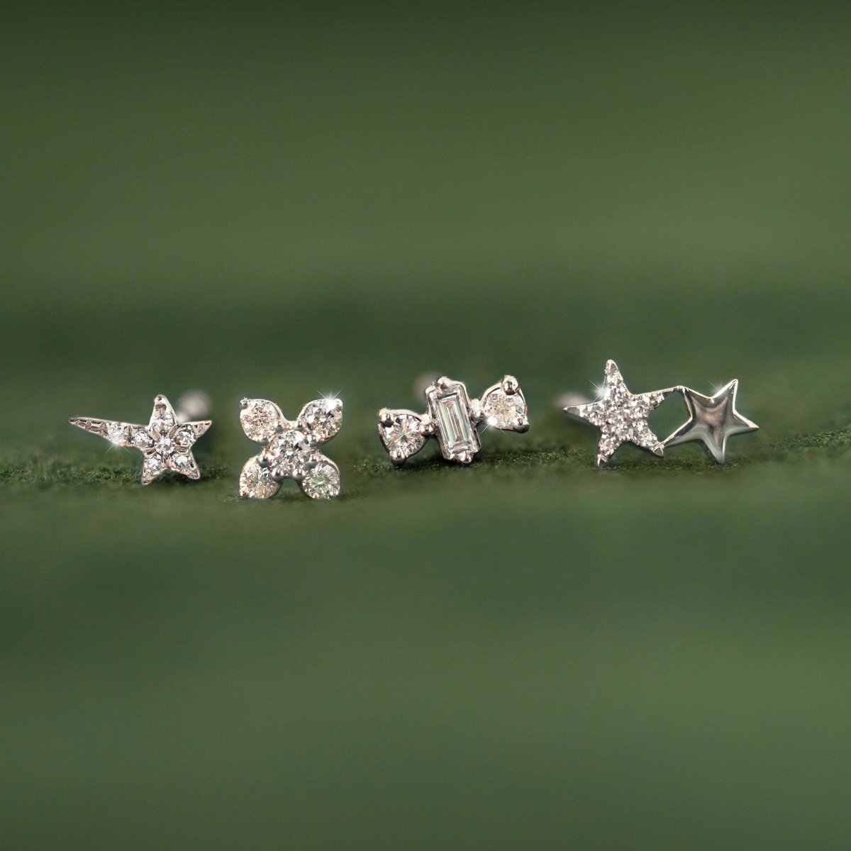 14K white gold diamond stud earrings in star, flower and baguette shapes, on a green surface