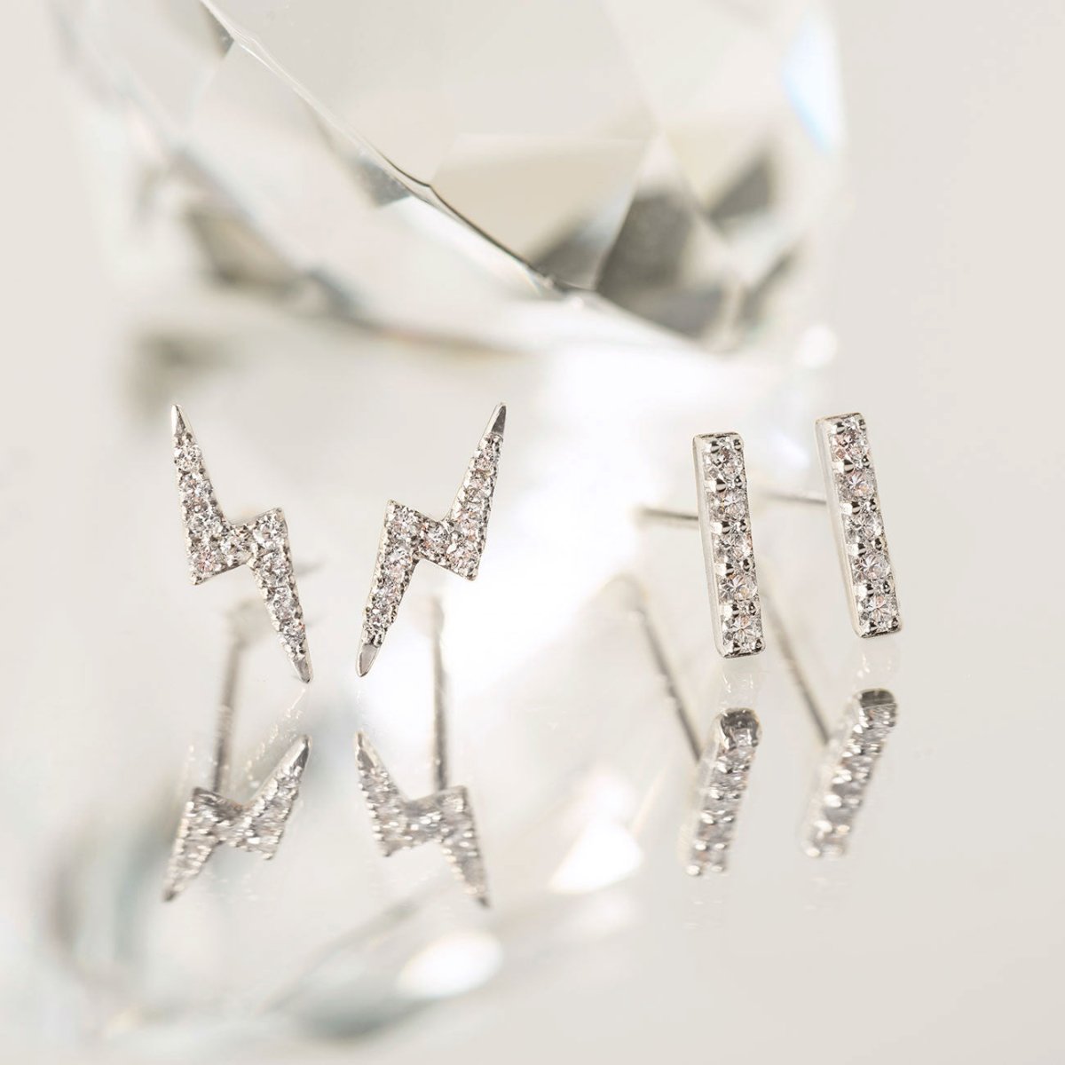 14K white gold lightning bolt pavé studs and bar studs with clear crystals, propped against a crystal
