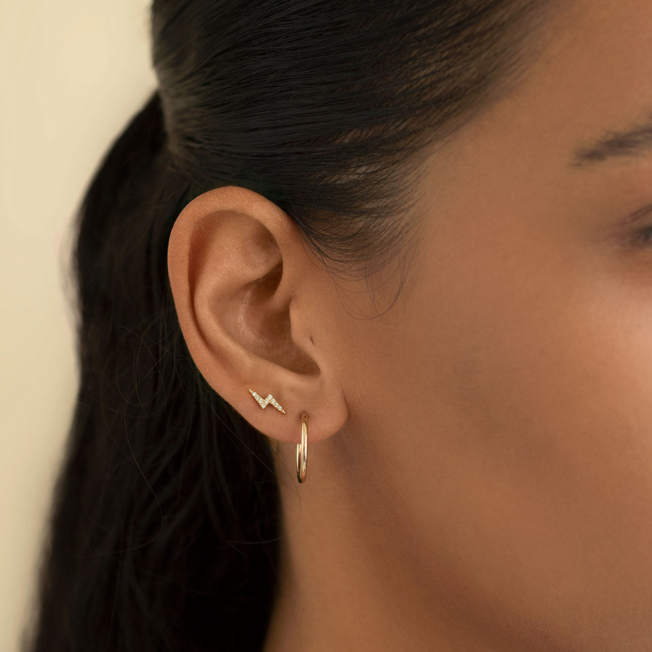 14K gold lightning bolt pavé stud with clear crystals shown on a model's lobe above a plain hoop