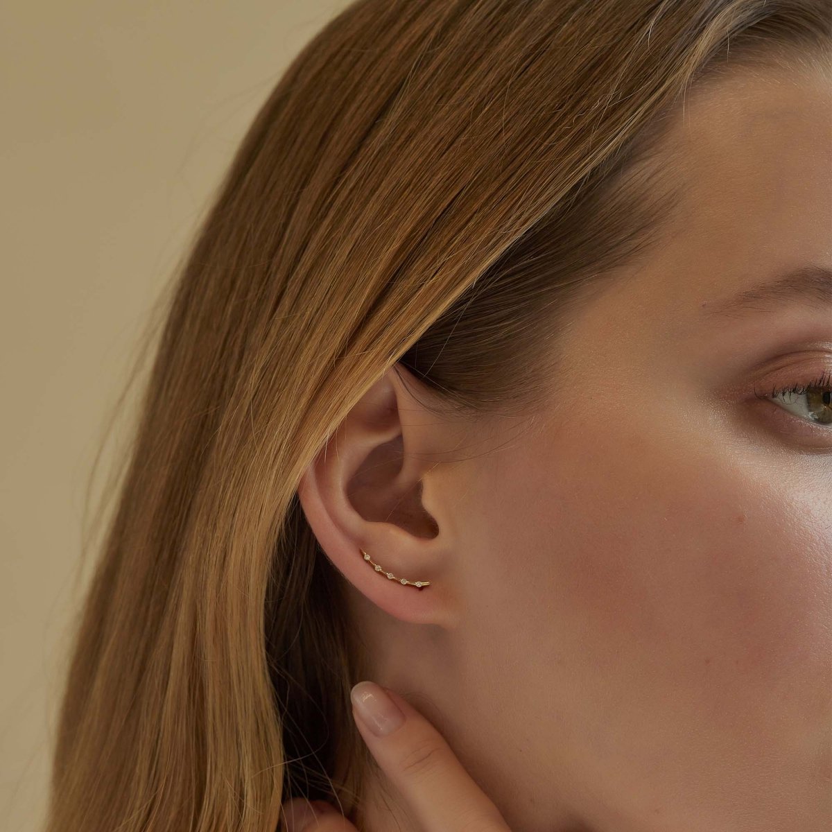 14K gold thin curved diamond climber traced along a model's lobe, close-up