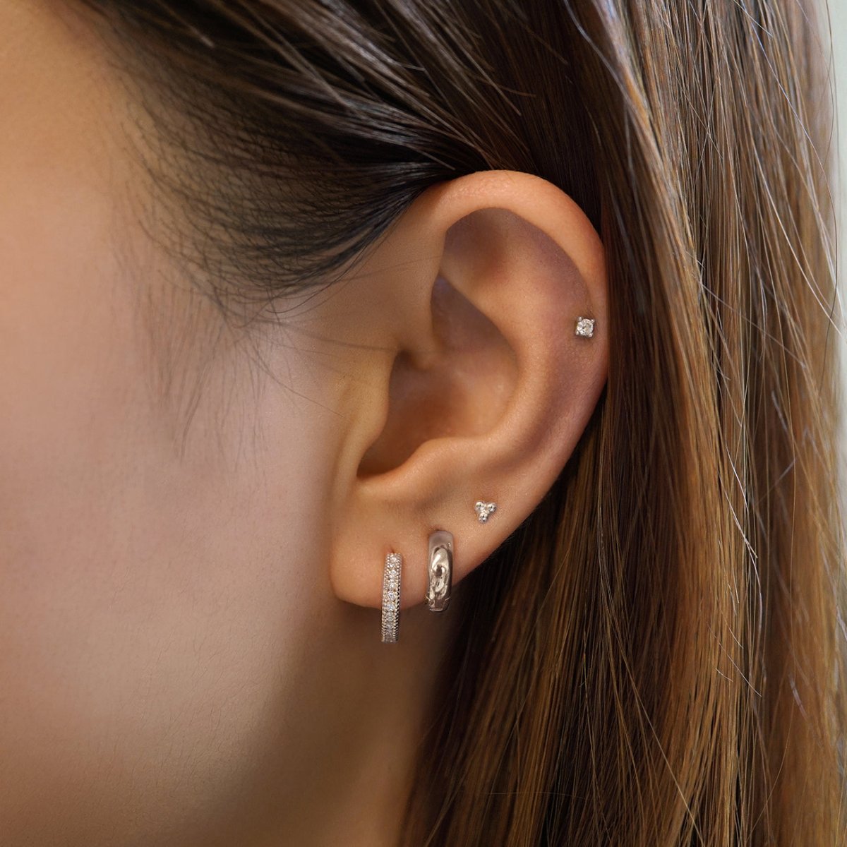 14K white gold milgrain diamond huggie shown on a model's lobe with a trio stud above