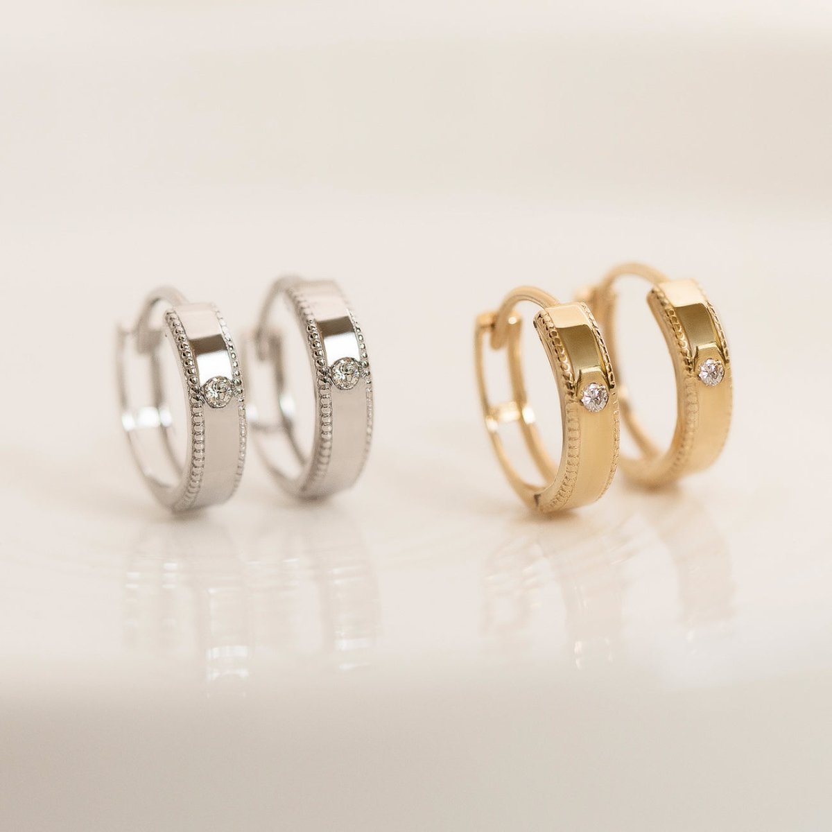 Silver and gold vermeil milgrain solitaire huggie hoops with round zirconia, on a cream background