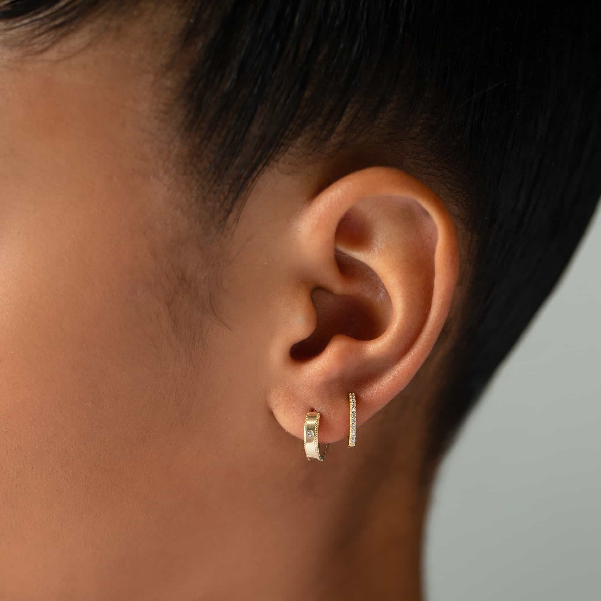 Gold vermeil milgrain band huggie with a clear solitaire stone, shown close-up on a model's lobe