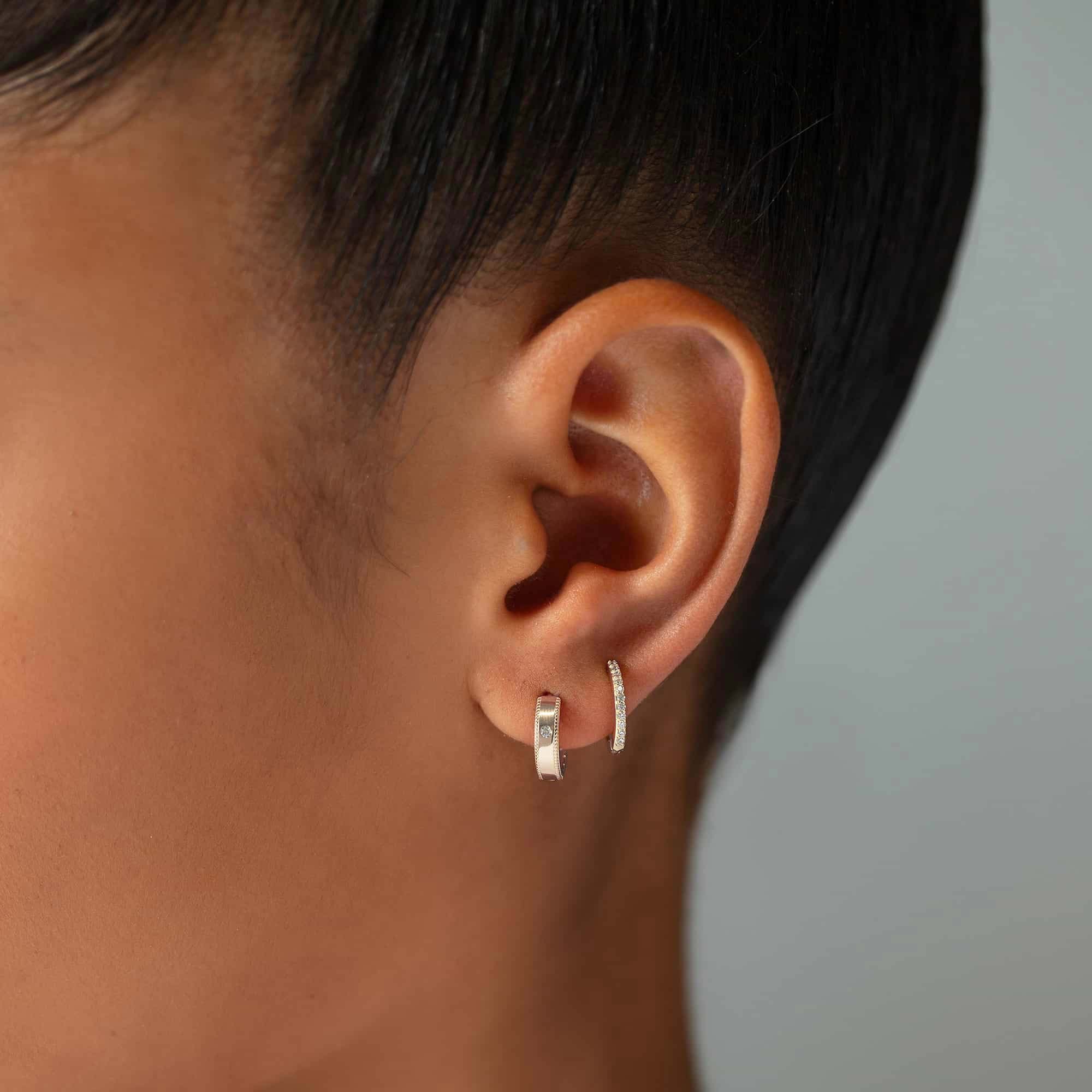 Two silver clear-stone huggie hoops shown stacked on a model's lobe