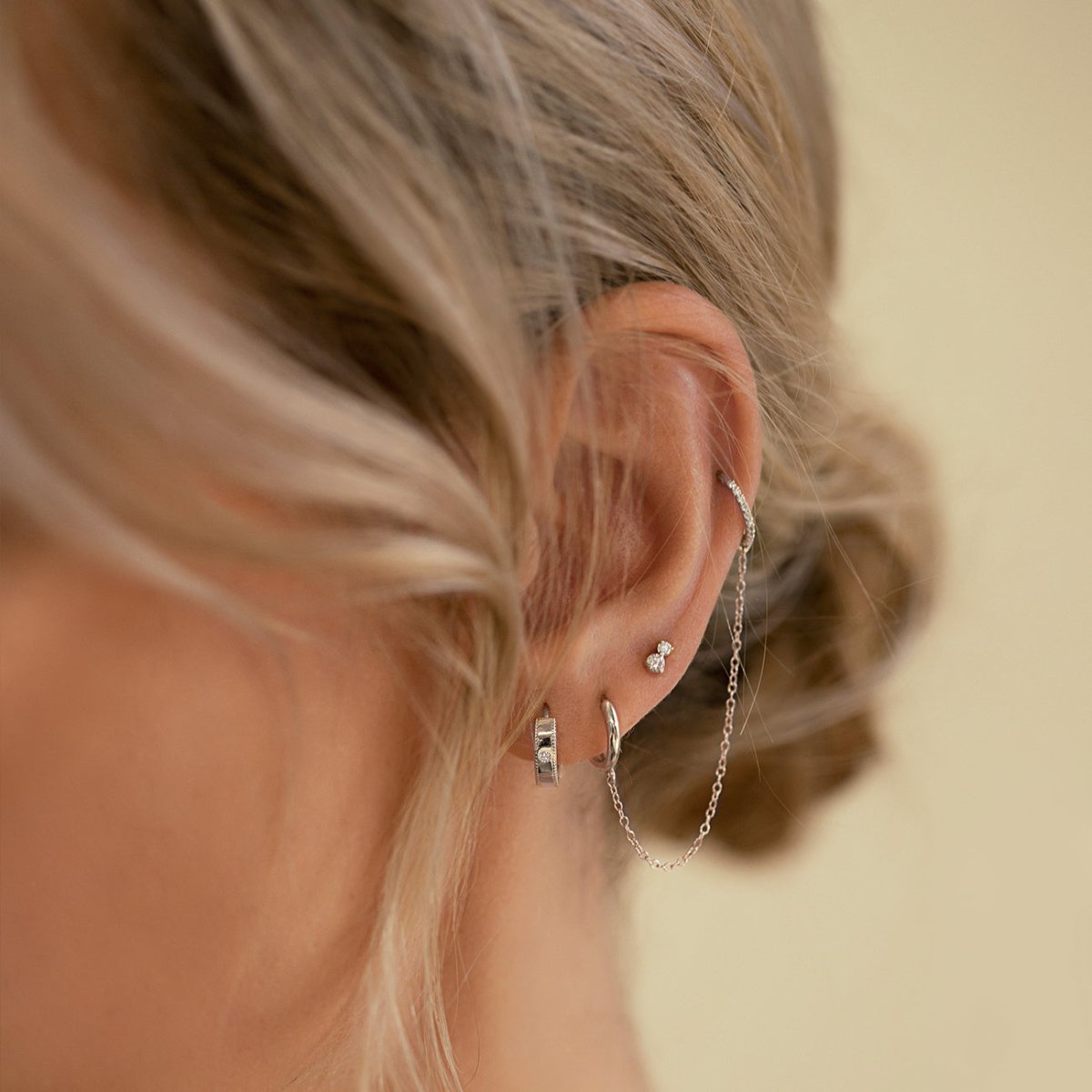 14K white gold milgrain diamond huggie hoop with a chain-linked stud, shown on a model's lobe and helix