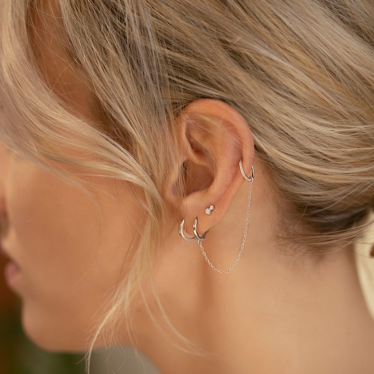 Titanium pavé cartilage hoop with white zirconia, shown on a model's ear styled in an ear stack