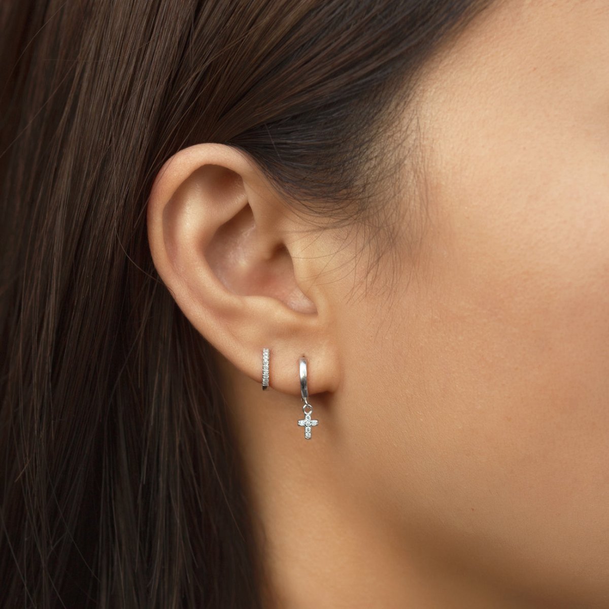 14K white gold pavé diamond huggie stacked with a hoop and a cross charm, on a model's lobe