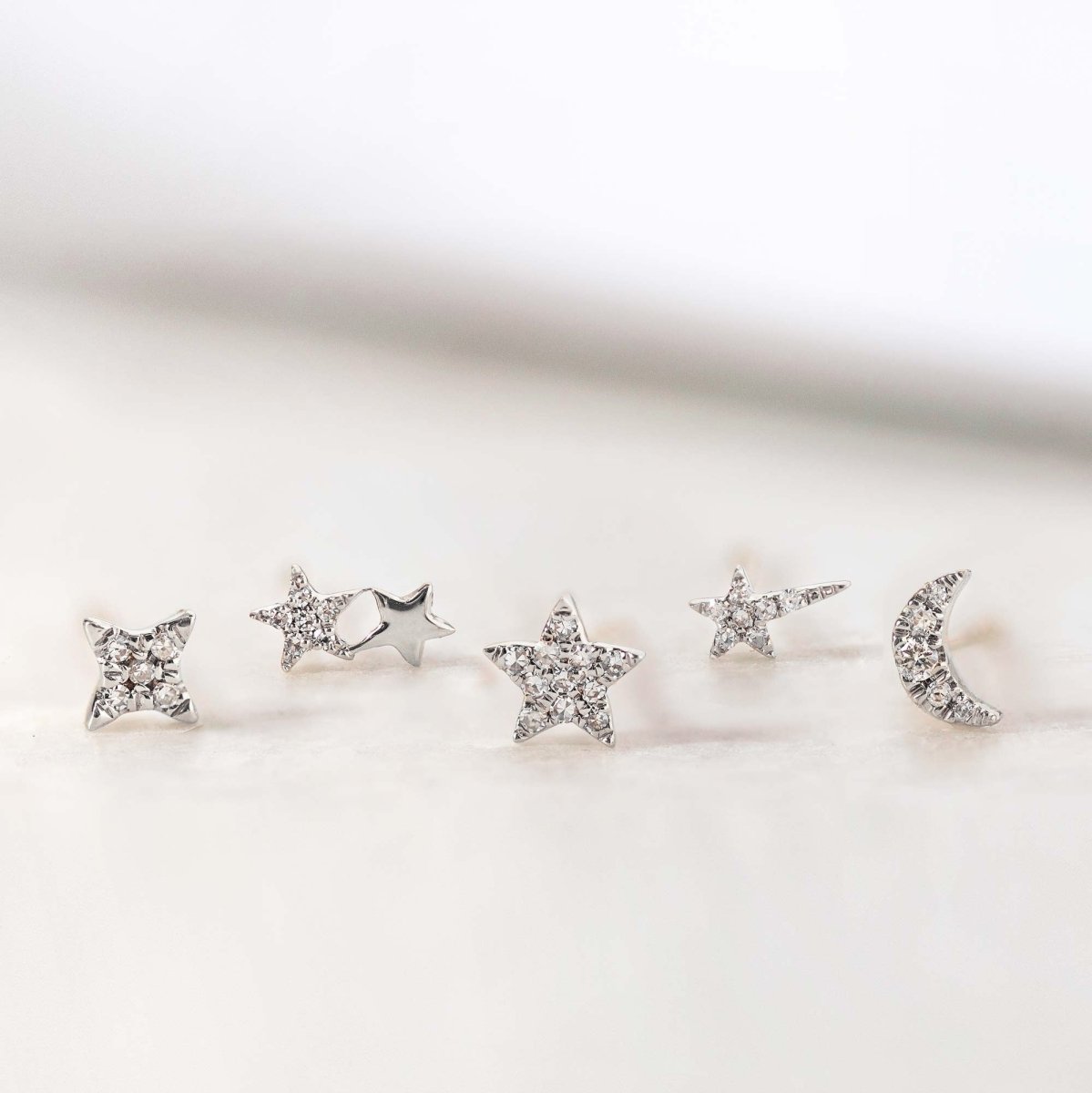 Row of silver star, four-point and crescent moon studs with clear stones, on a cream background