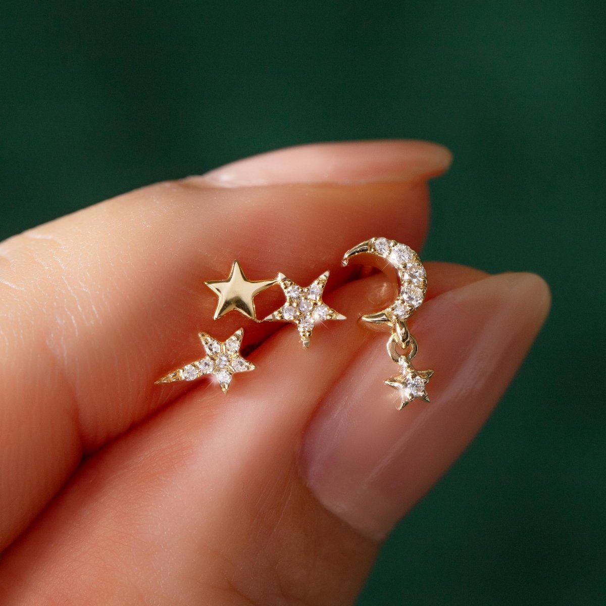 14K gold star and crescent moon diamond stud earrings with a dangling star, held in fingers