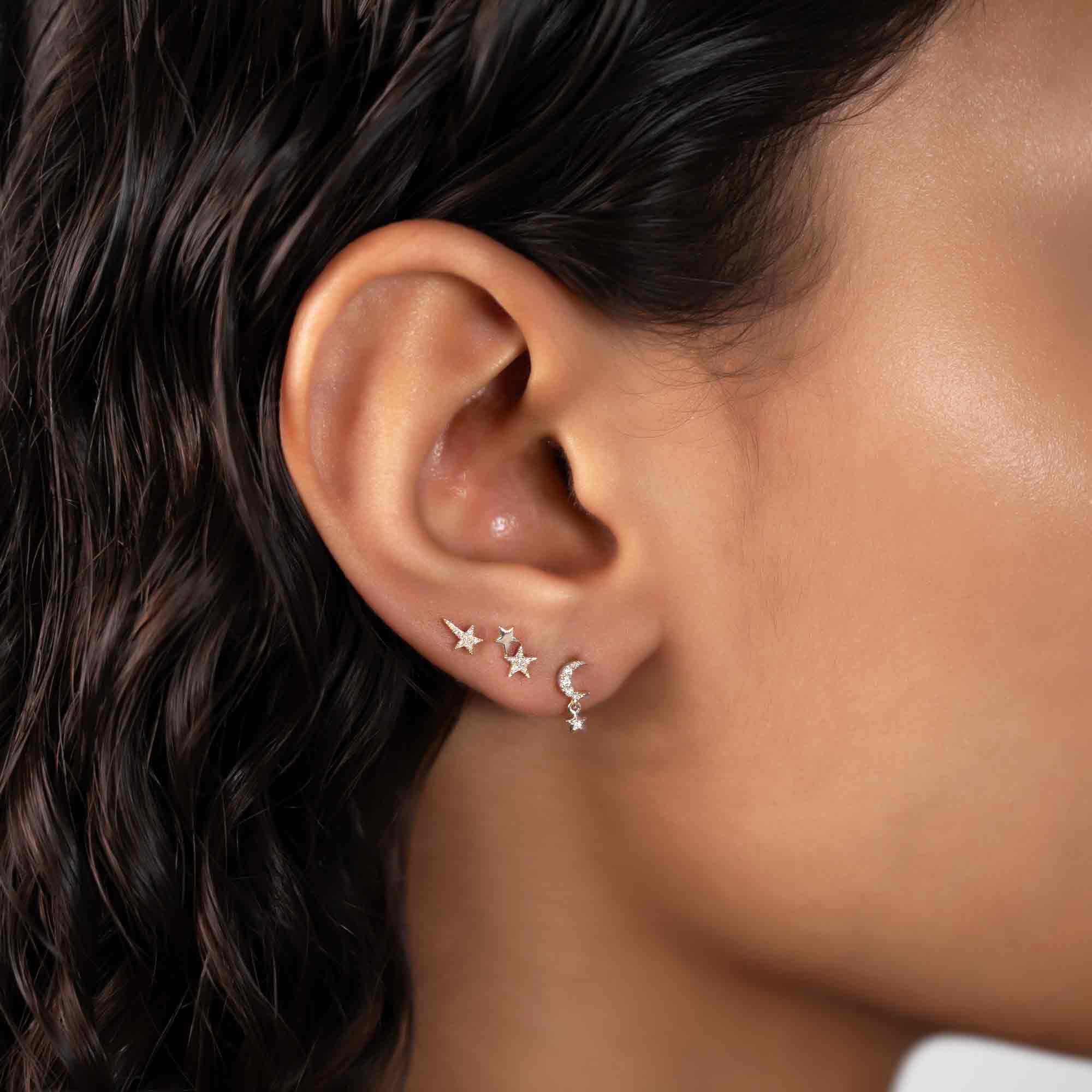 Silver crescent moon and star studs with clear stones and a dangling star, on a model's lobe