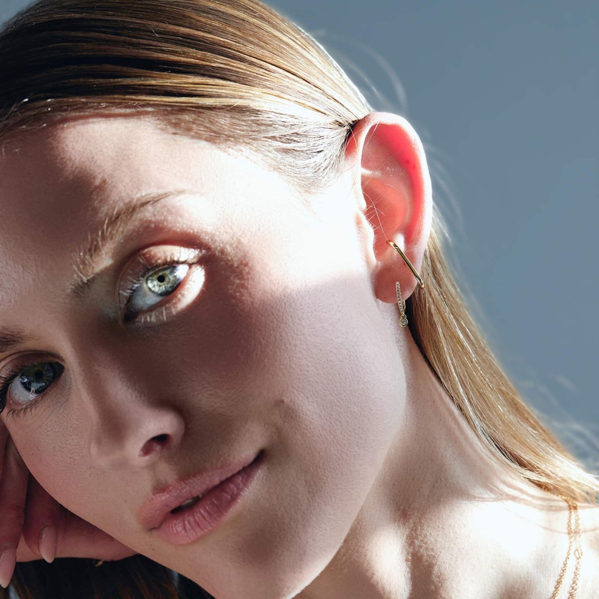 14K gold thin diamond drop huggie shown on a model's lobe in a close-up profile