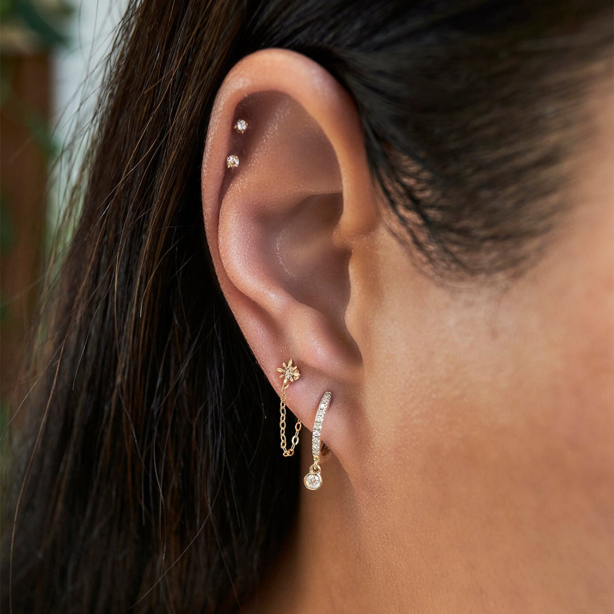 14K gold starburst single stud with a white zirconia, shown chained to a lobe huggie on a model