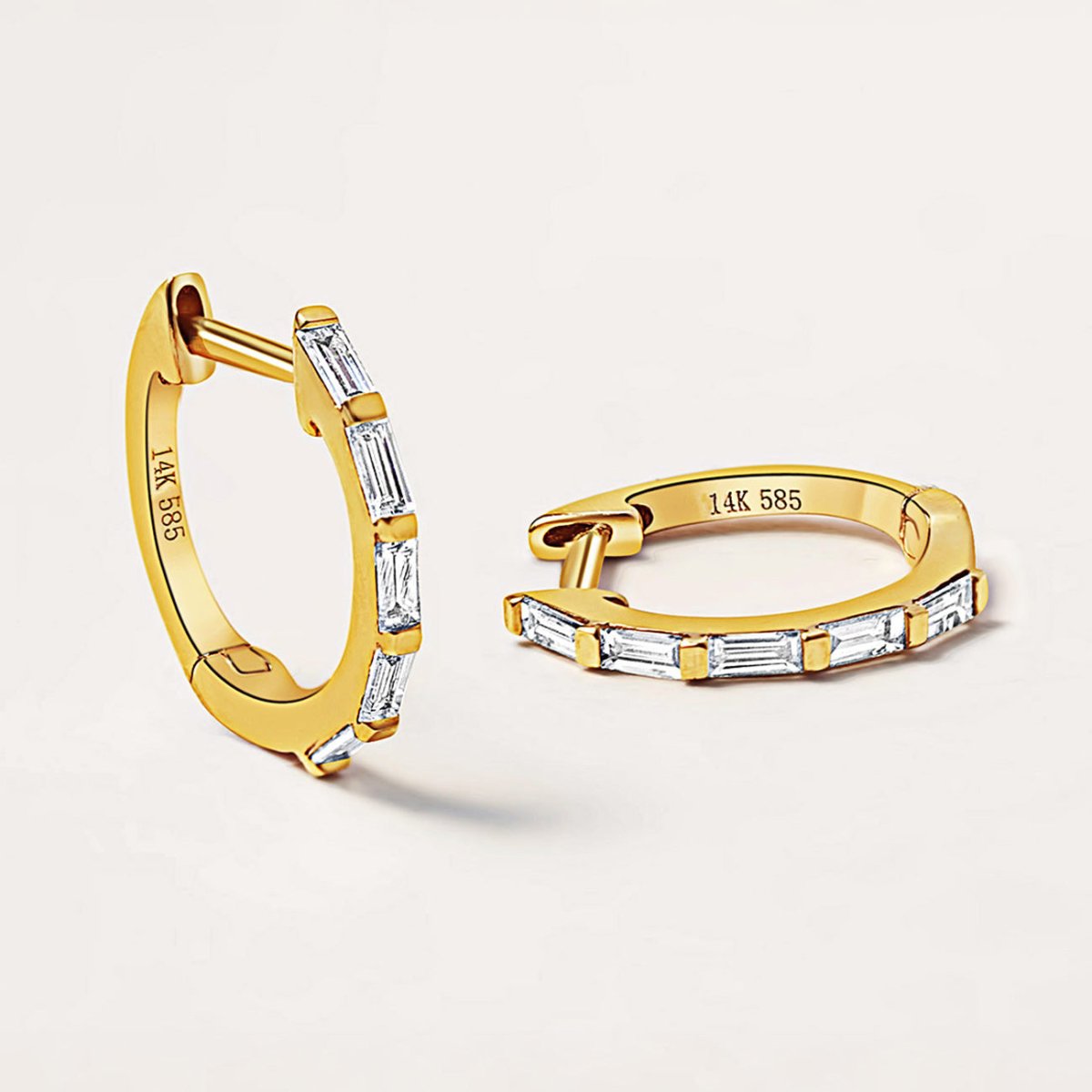 14K gold baguette diamond huggie hoops with clear stones, close-up detail of the pair on a cream background