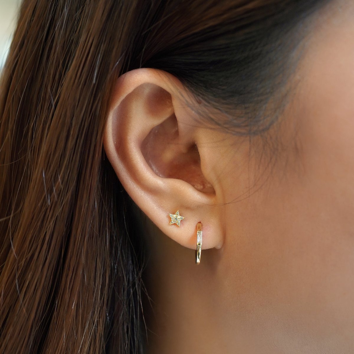 14K gold baguette diamond huggie hoop shown on a model's lobe below a star stud