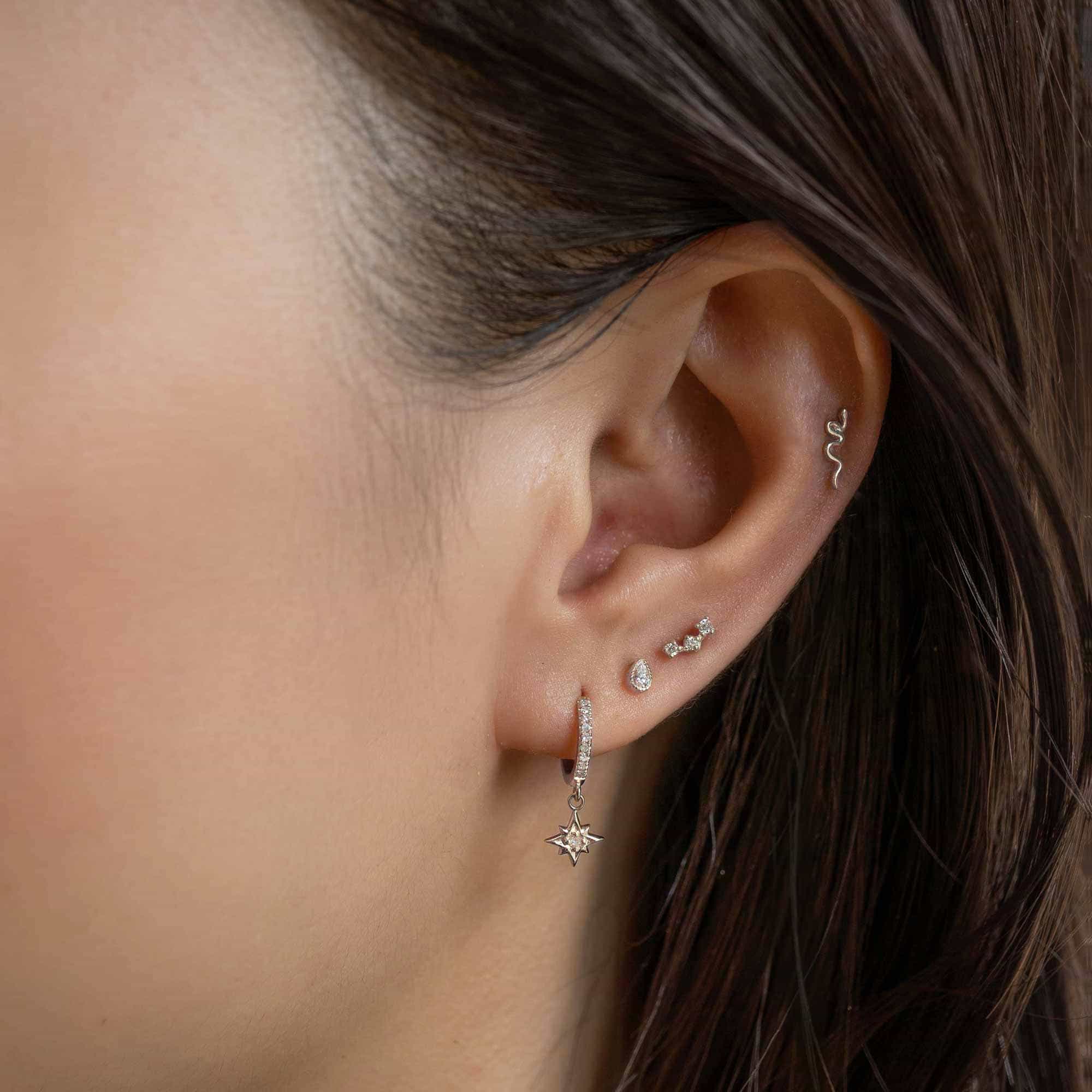14K white gold diamond starburst pavé huggie hoop shown on a model's lobe among stacked piercings