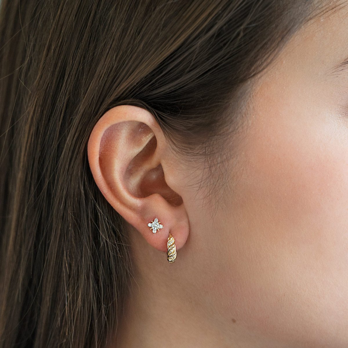 Gold clear-stone starburst stud and a twisted huggie hoop shown on a model's lobe
