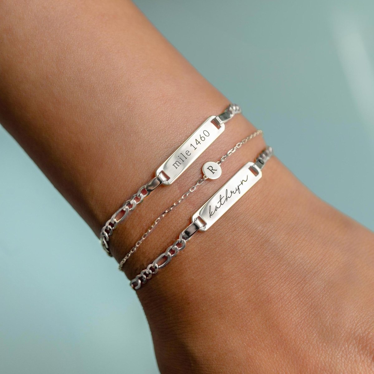 Sterling silver disc bracelet engraved with an initial, shown stacked with ID bracelets on a wrist