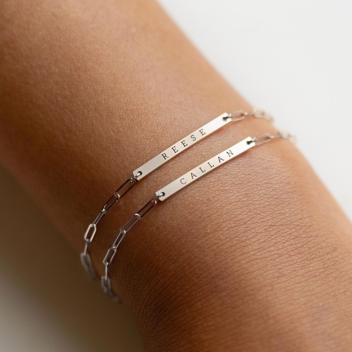 Two sterling silver thin bar paperclip chain bracelets engraved with names, on a model's wrist