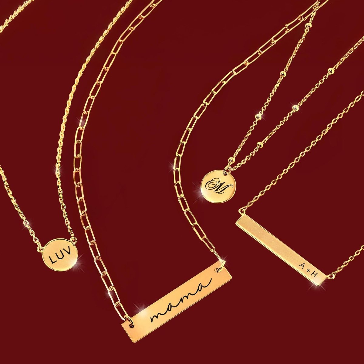 Gold vermeil bar and disc necklaces engraved with names and initials, layered on a deep red background