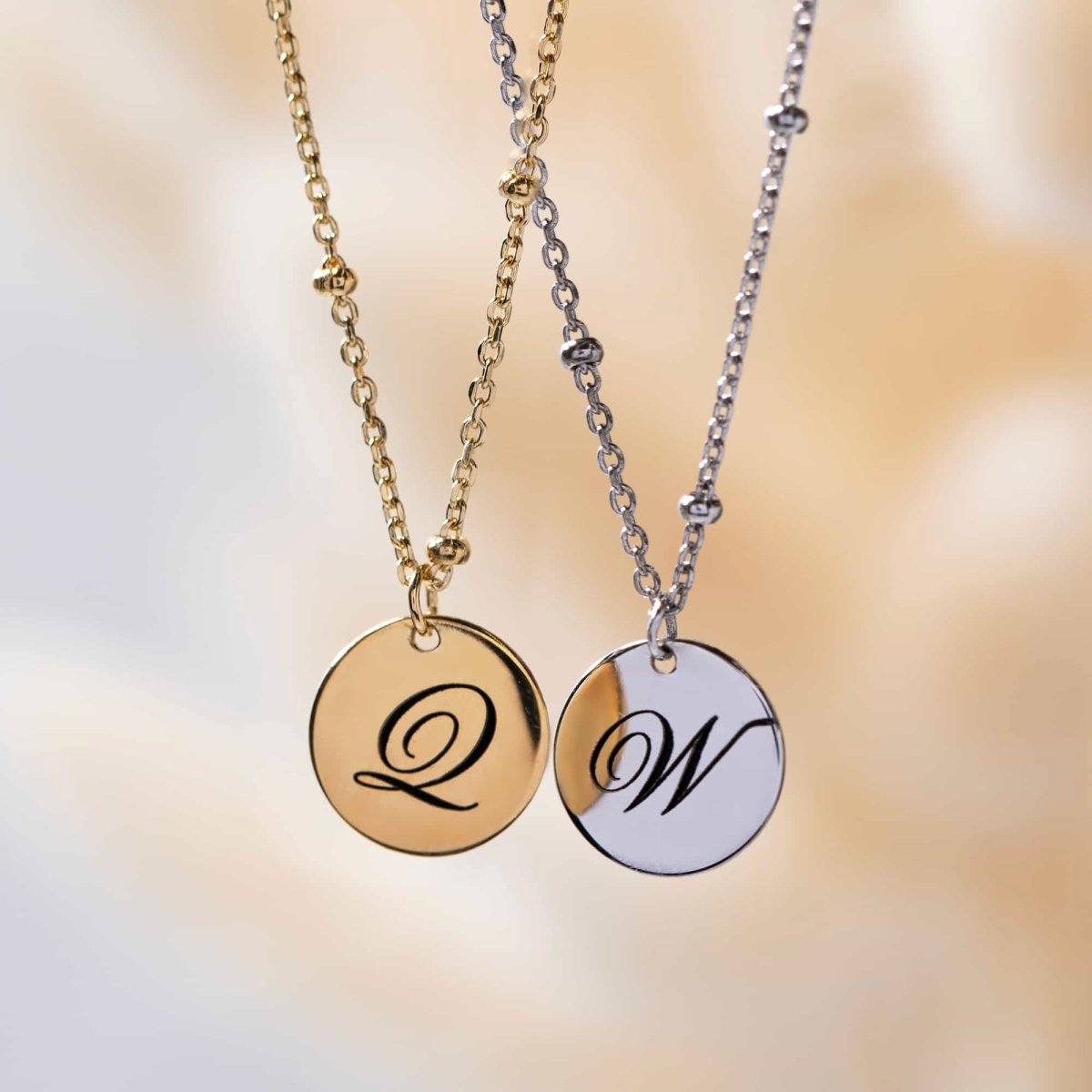 Sterling silver initial disc bead chain necklace engraved with an initial, beside a gold pair