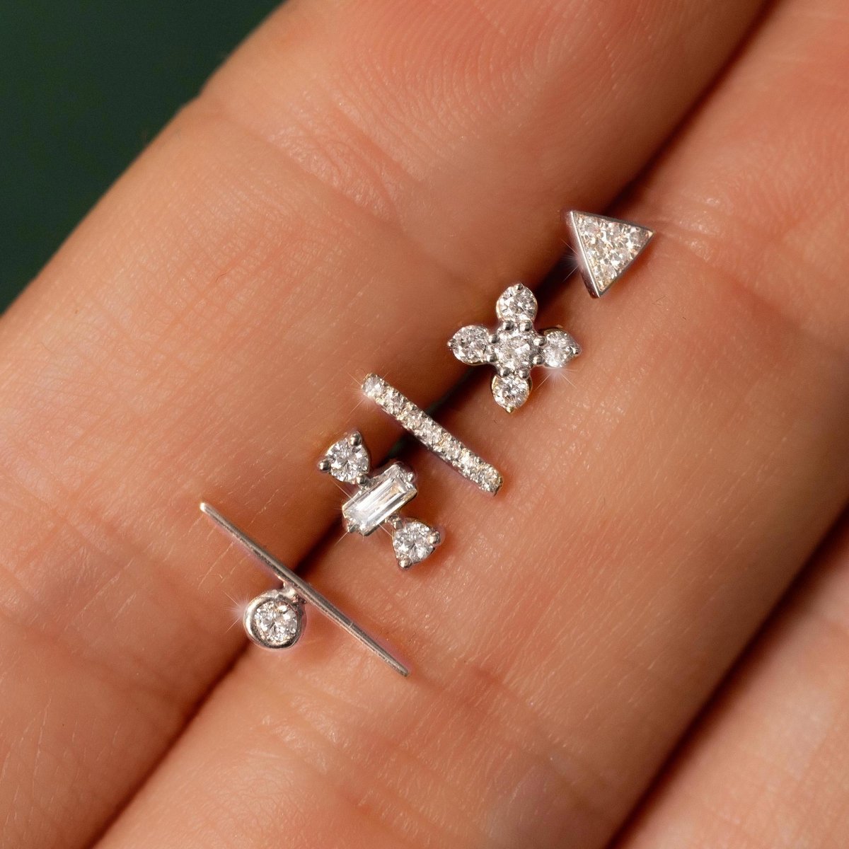 14K white gold tiny triangle stud with clear stones, shown loose on a fingertip with other studs