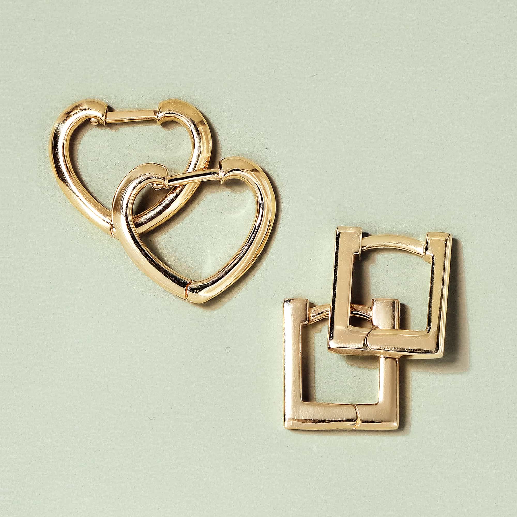 14K gold square huggie earrings beside gold heart-shaped huggies, on a sage green background