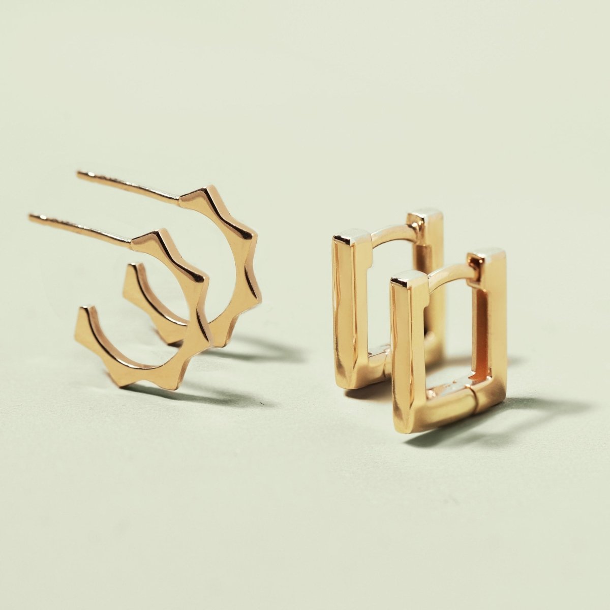 14K gold sunray C hoops with a faceted open profile, shown beside square huggies on a cream background