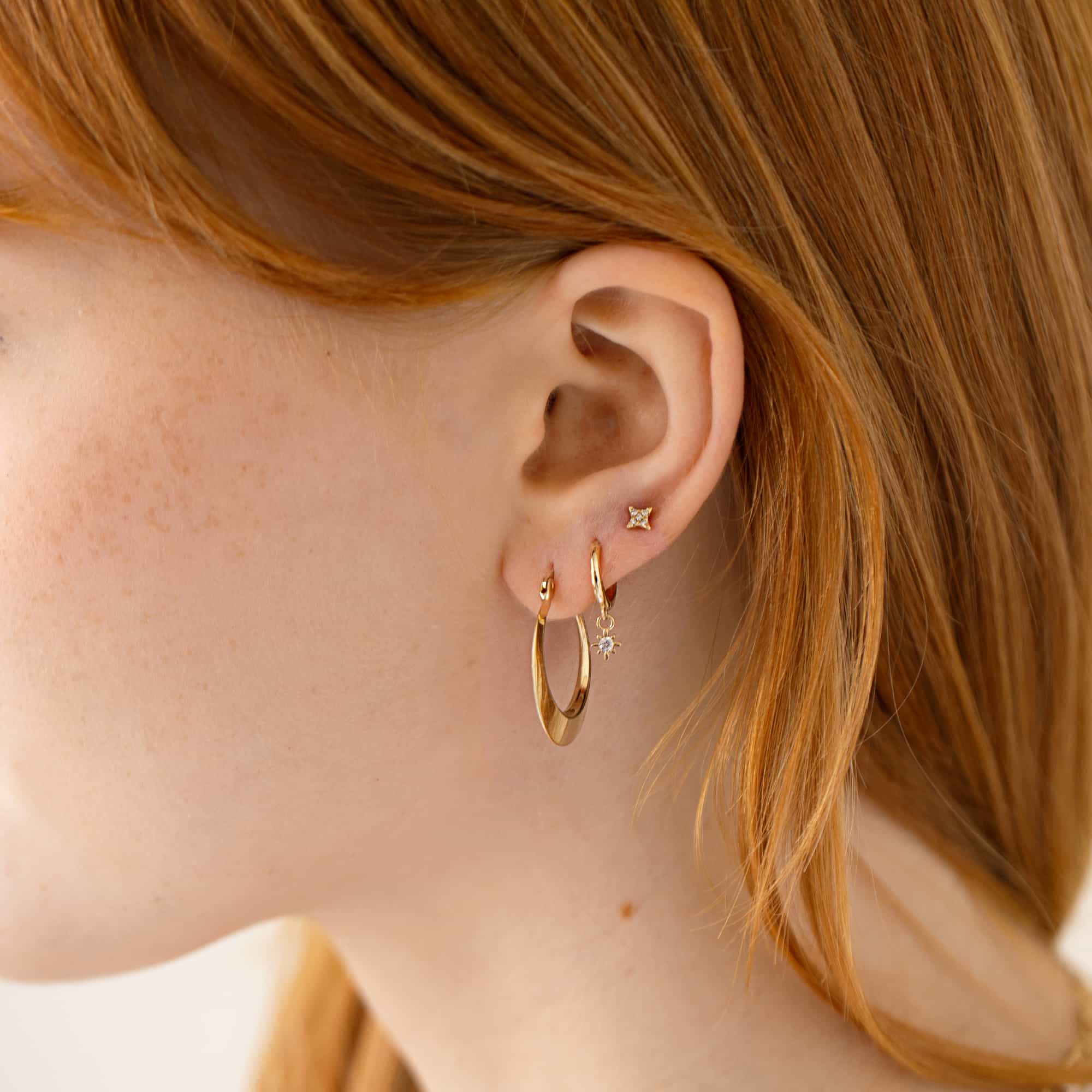 Gold hoop with a starburst charm and a clear-stone stud shown on a model's lobe
