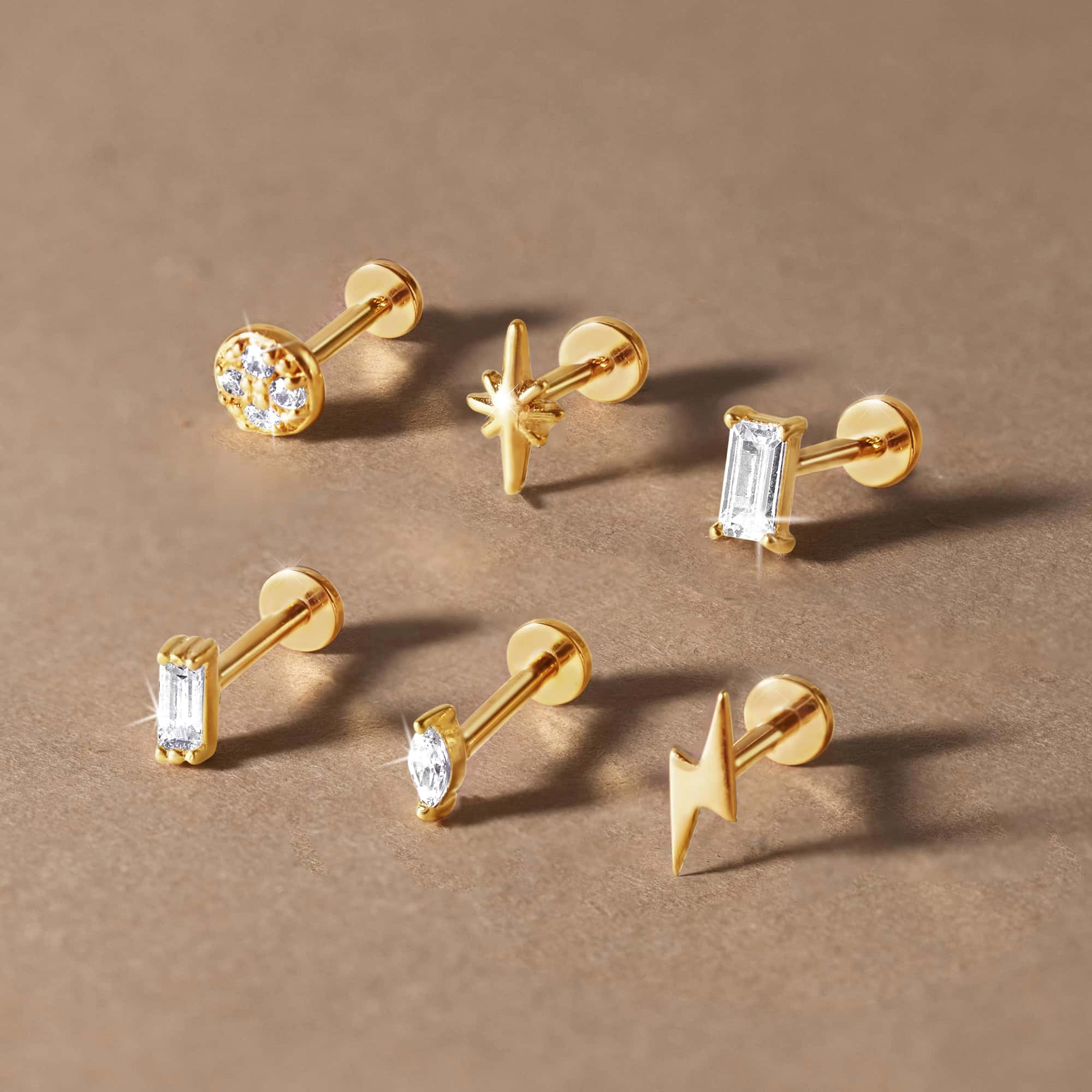Assortment of gold flat back studs, including pavé, star, bolt and baguette, on a tan surface