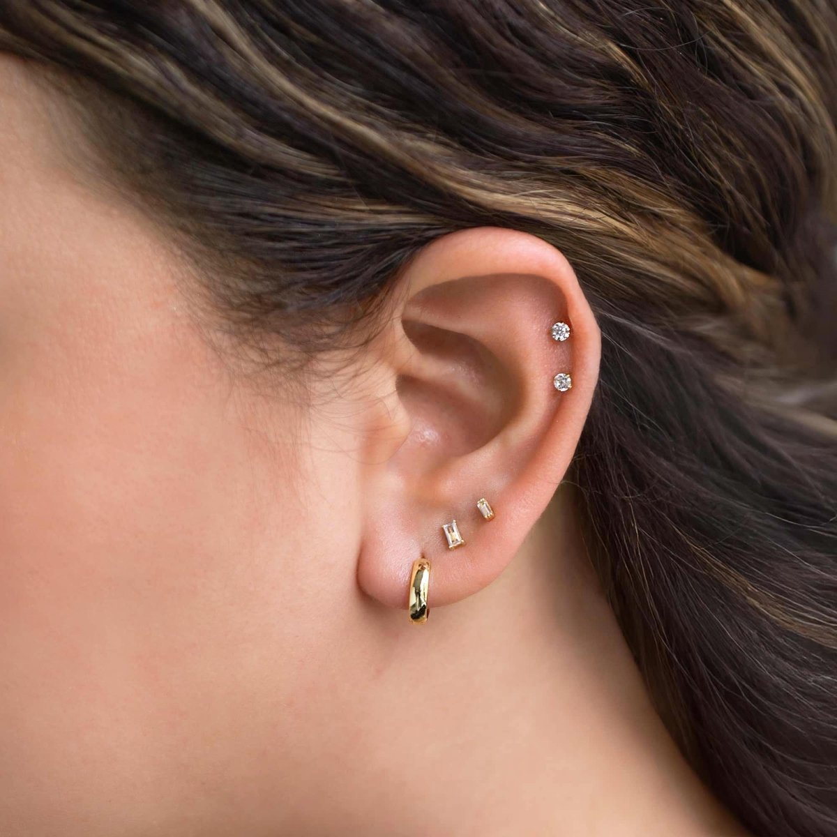Gold baguette flat back stud with clear stone styled with a hoop in an ear stack on a model