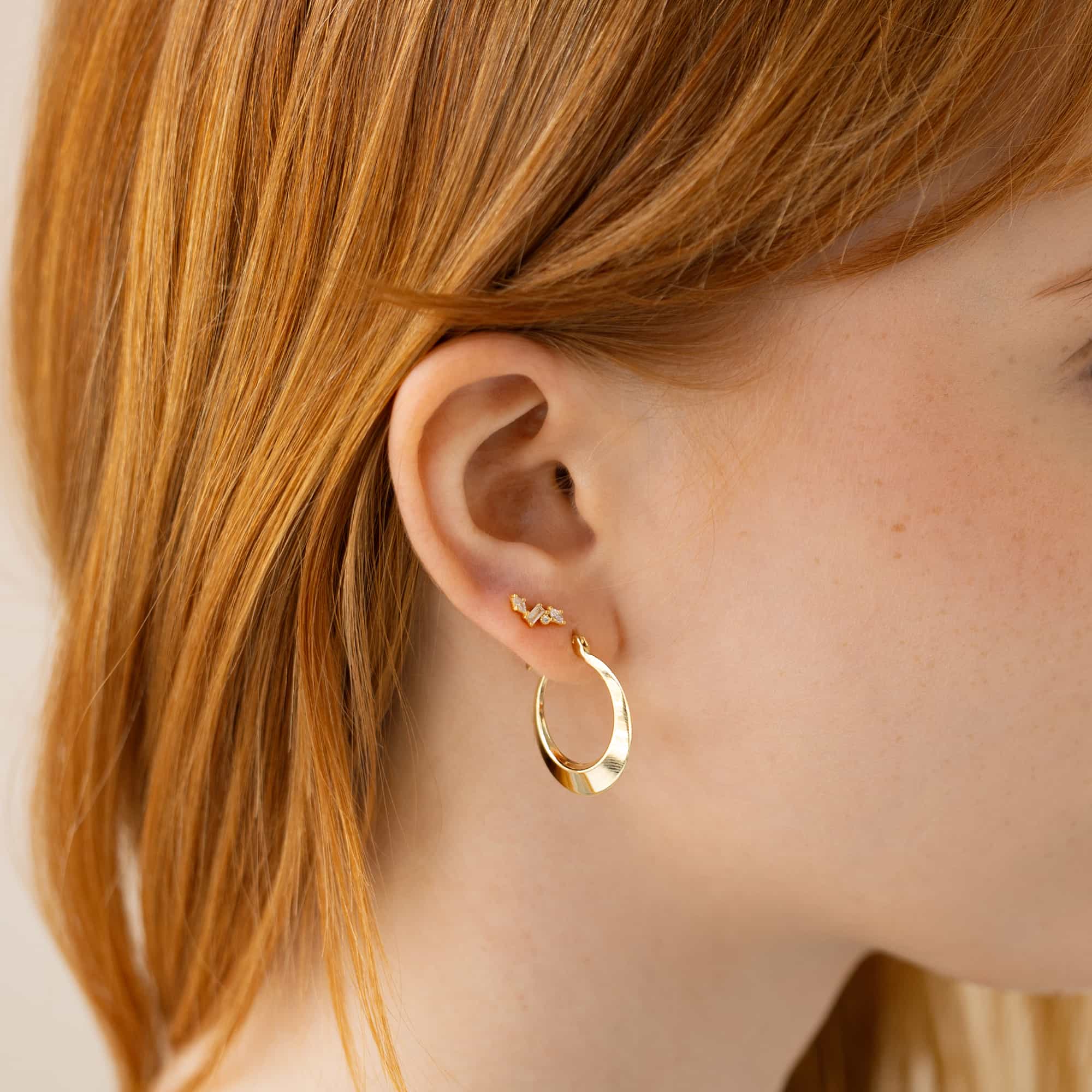 Gold tapered hoop and a clear-stone cluster stud shown on a model's ear