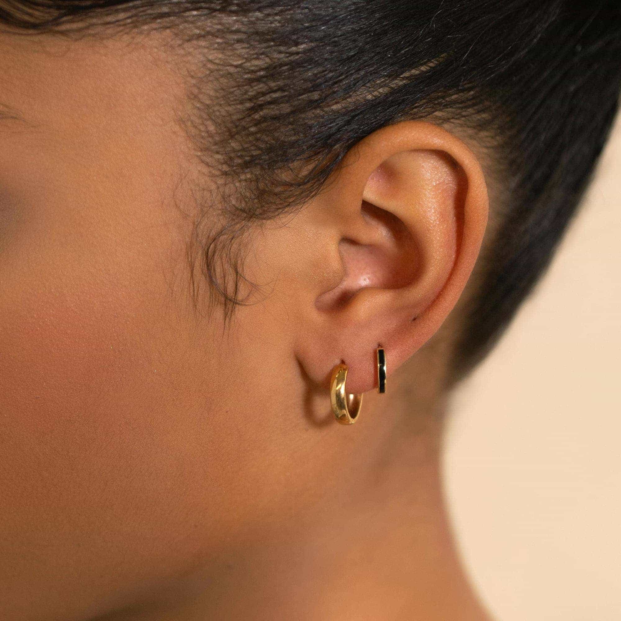 14K gold thin mini huggie hoops shown on a model's lobe