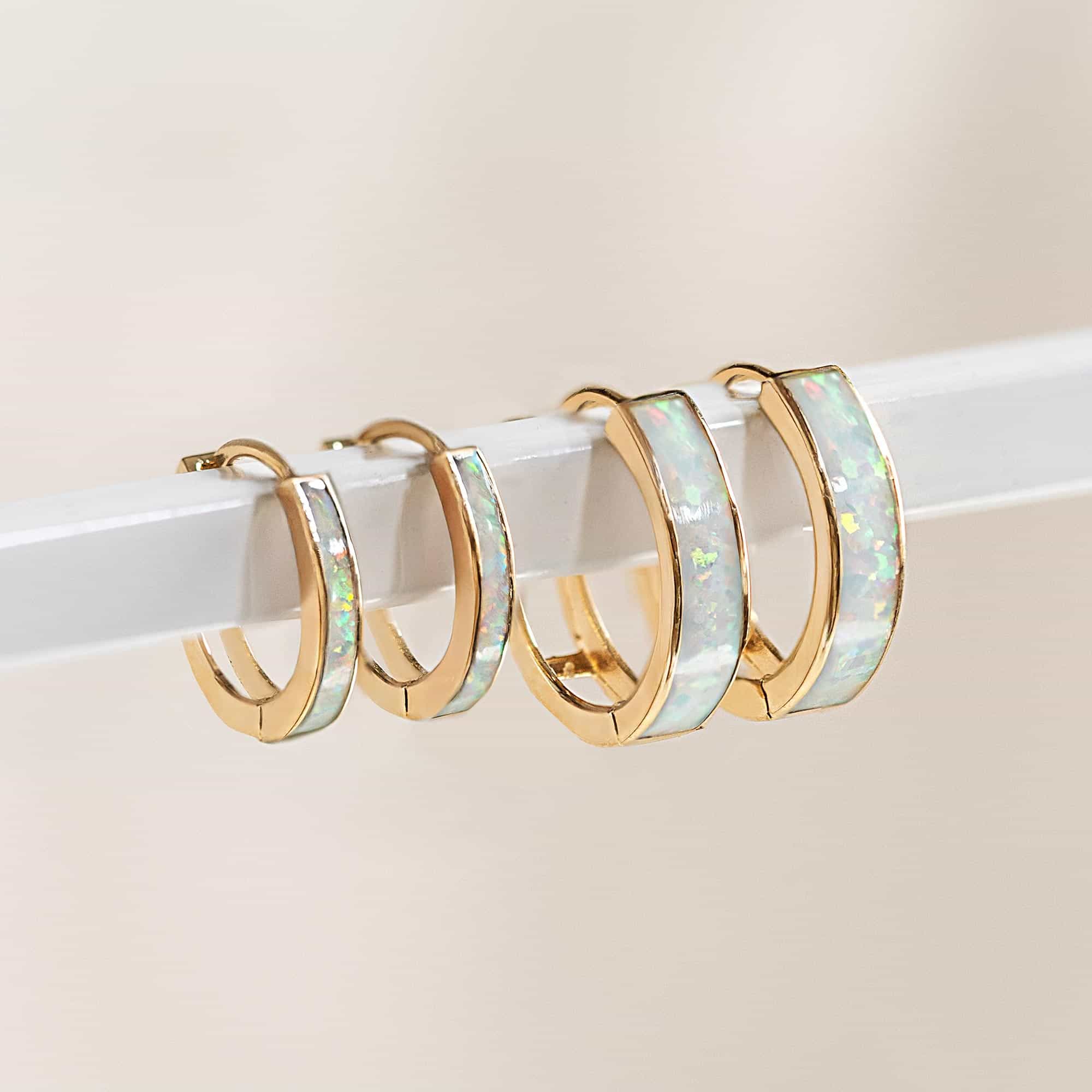 14K gold white opal huggie hoops in two sizes, lined up on a clear acrylic bar
