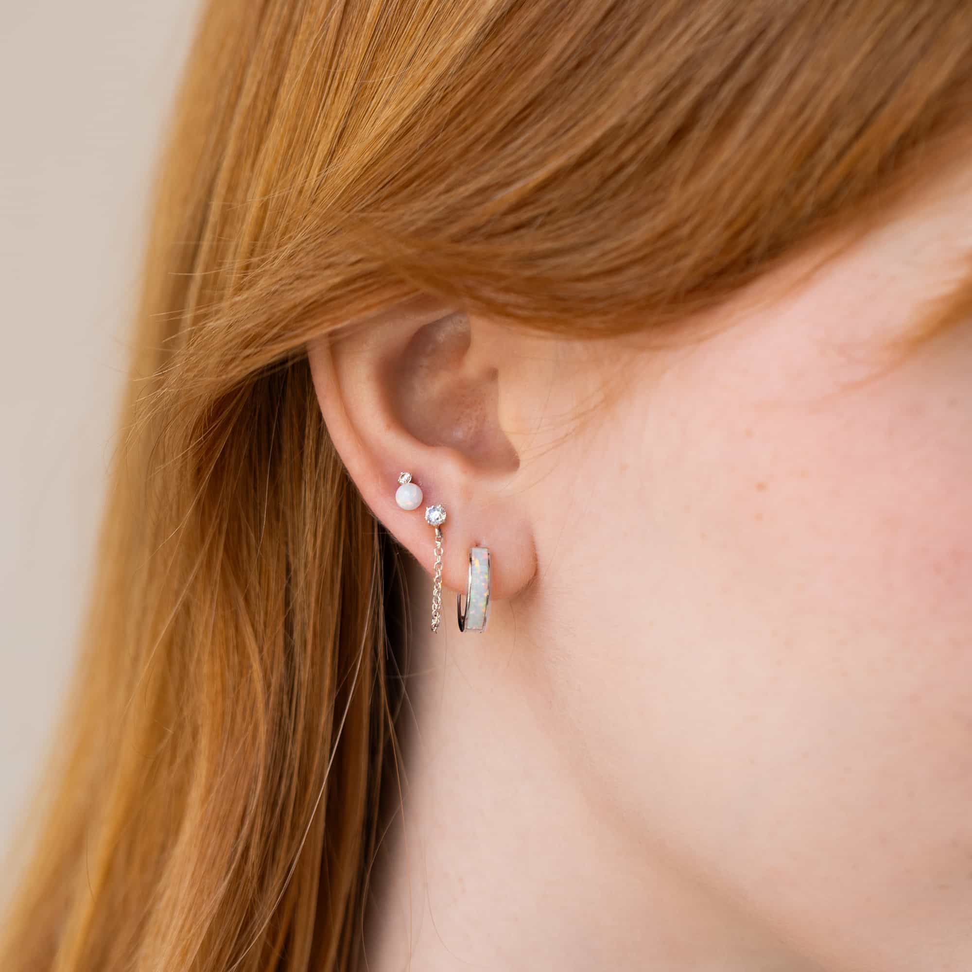 Close-up of woman's ear featuring 14K White Gold Tiny Sapphire and Chain Studs paired with opal earrings 