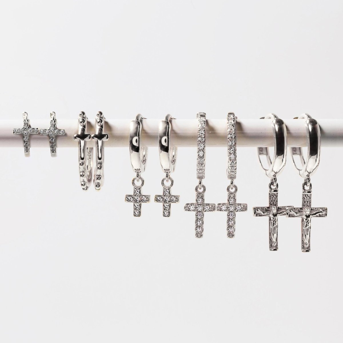 14K white gold cross drop huggie hoops shown in a lineup of cross earring styles, on a white background