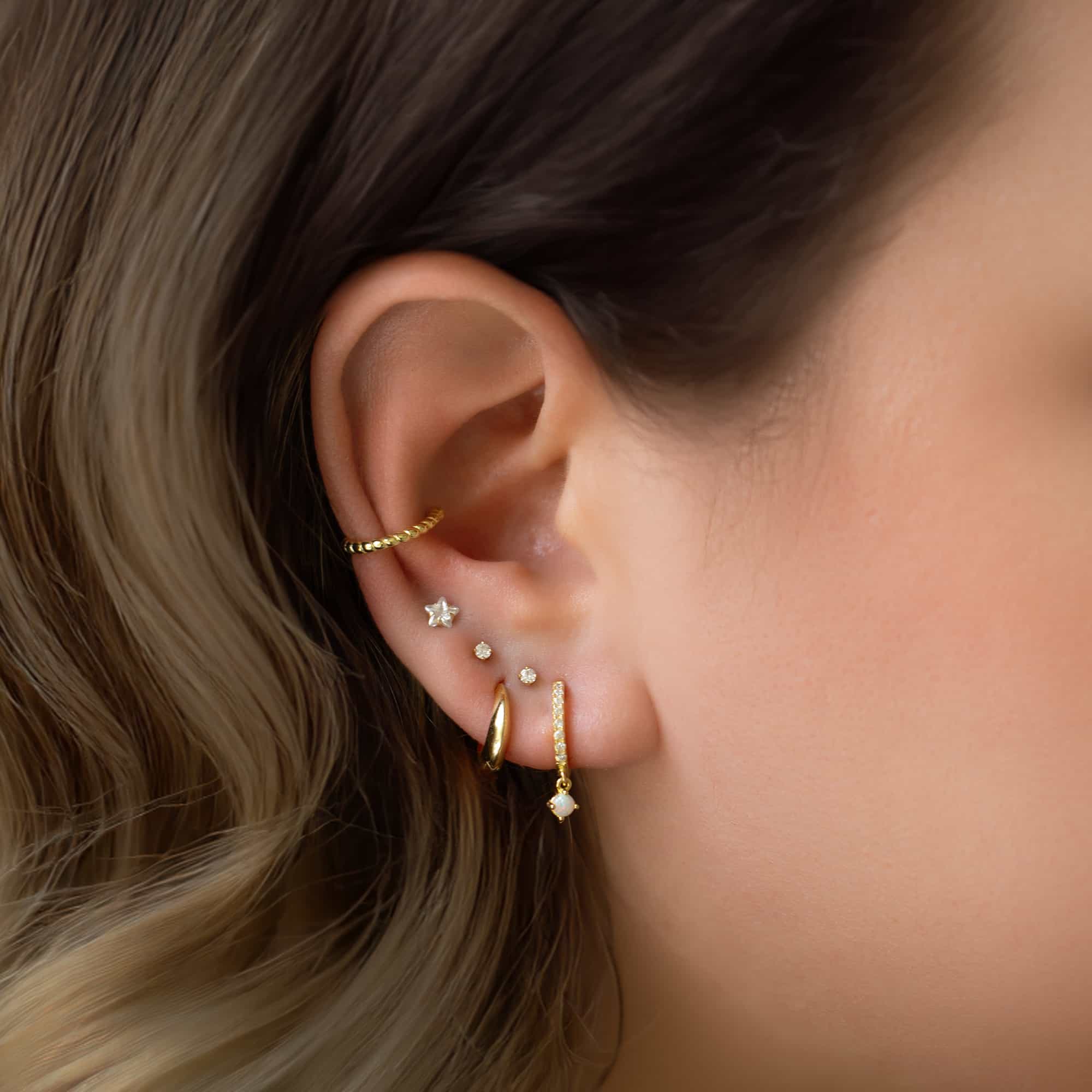 Gold vermeil pavé huggie hoop with a white opal drop, shown in a stacked ear with a star stud and cuff