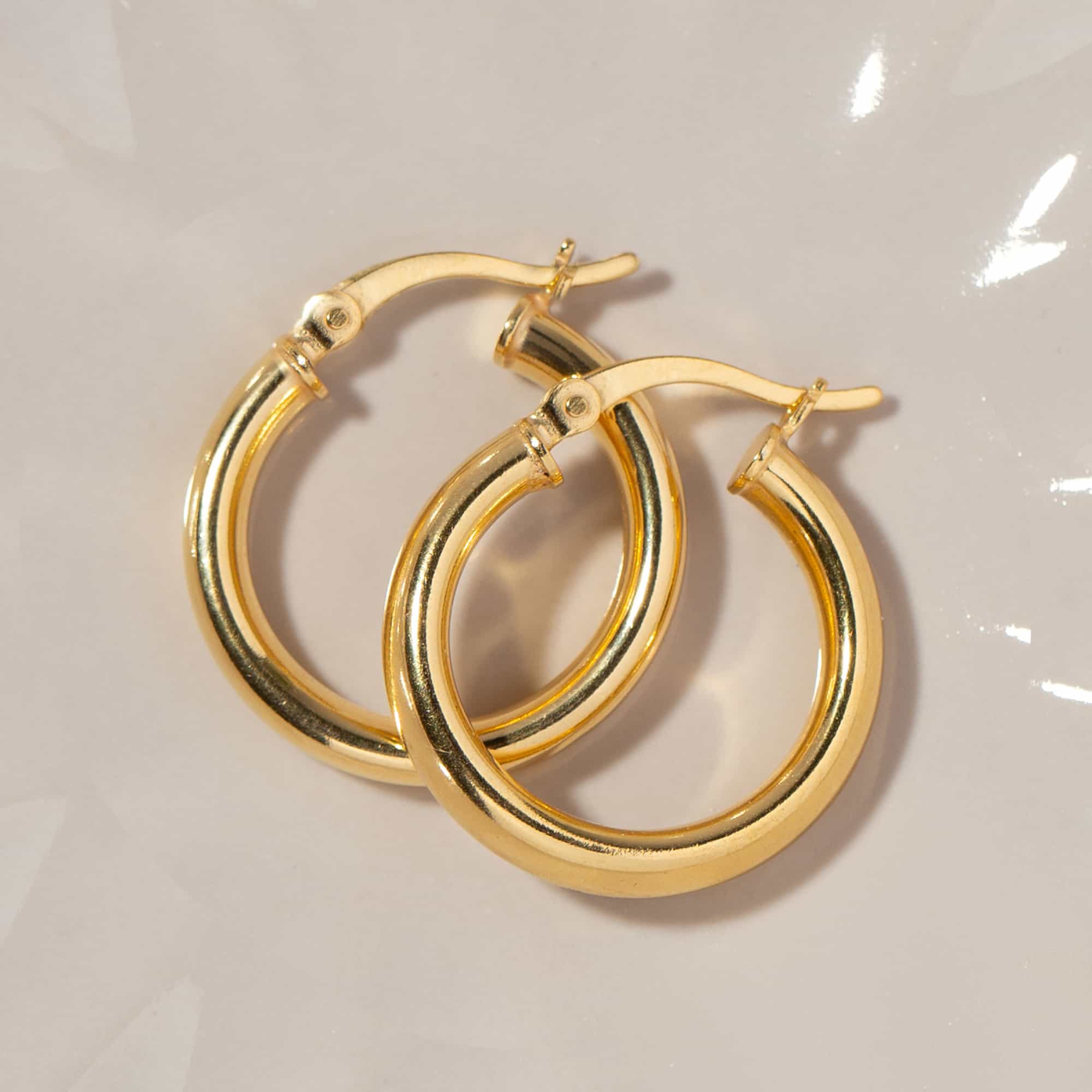 Gold vermeil thick tube hoop earrings laid on a cream surface, close-up detail