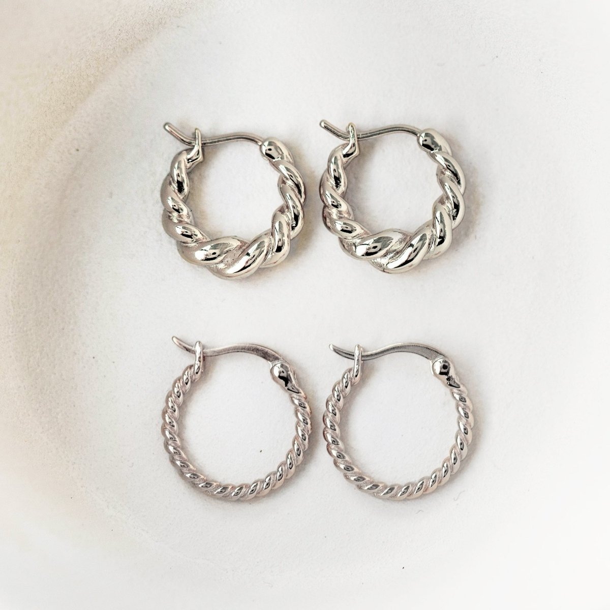 Sterling silver twisted rope hoop earrings in two sizes, laid on a cream dish
