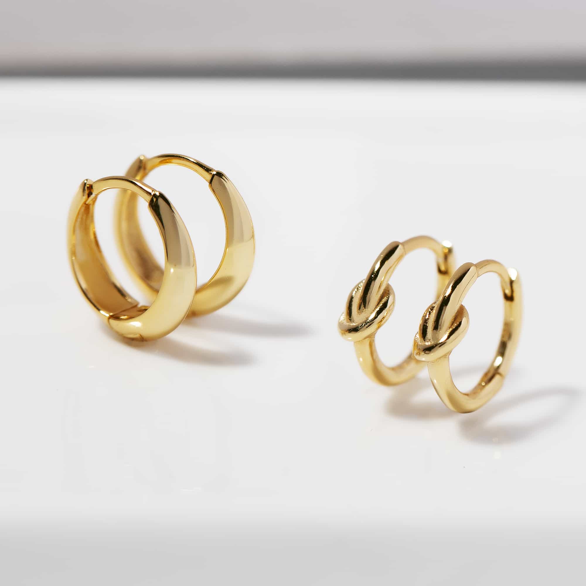 Two pairs of gold huggie hoops, one domed and one knotted, on a white background
