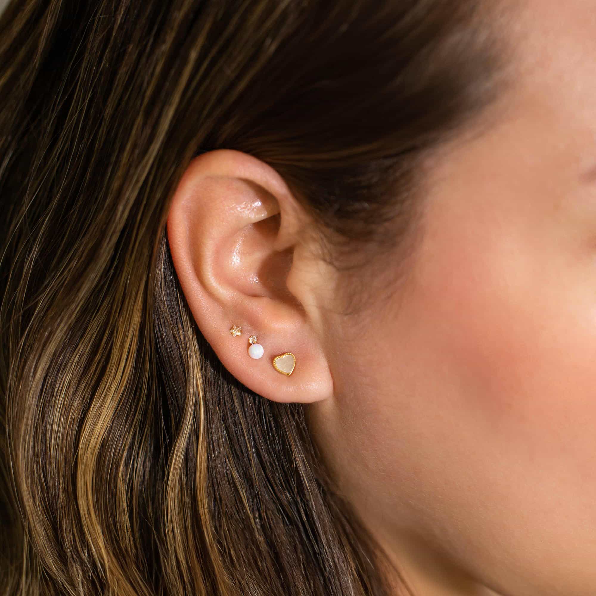 Gold star stud and opal heart stud shown on a model's lobe
